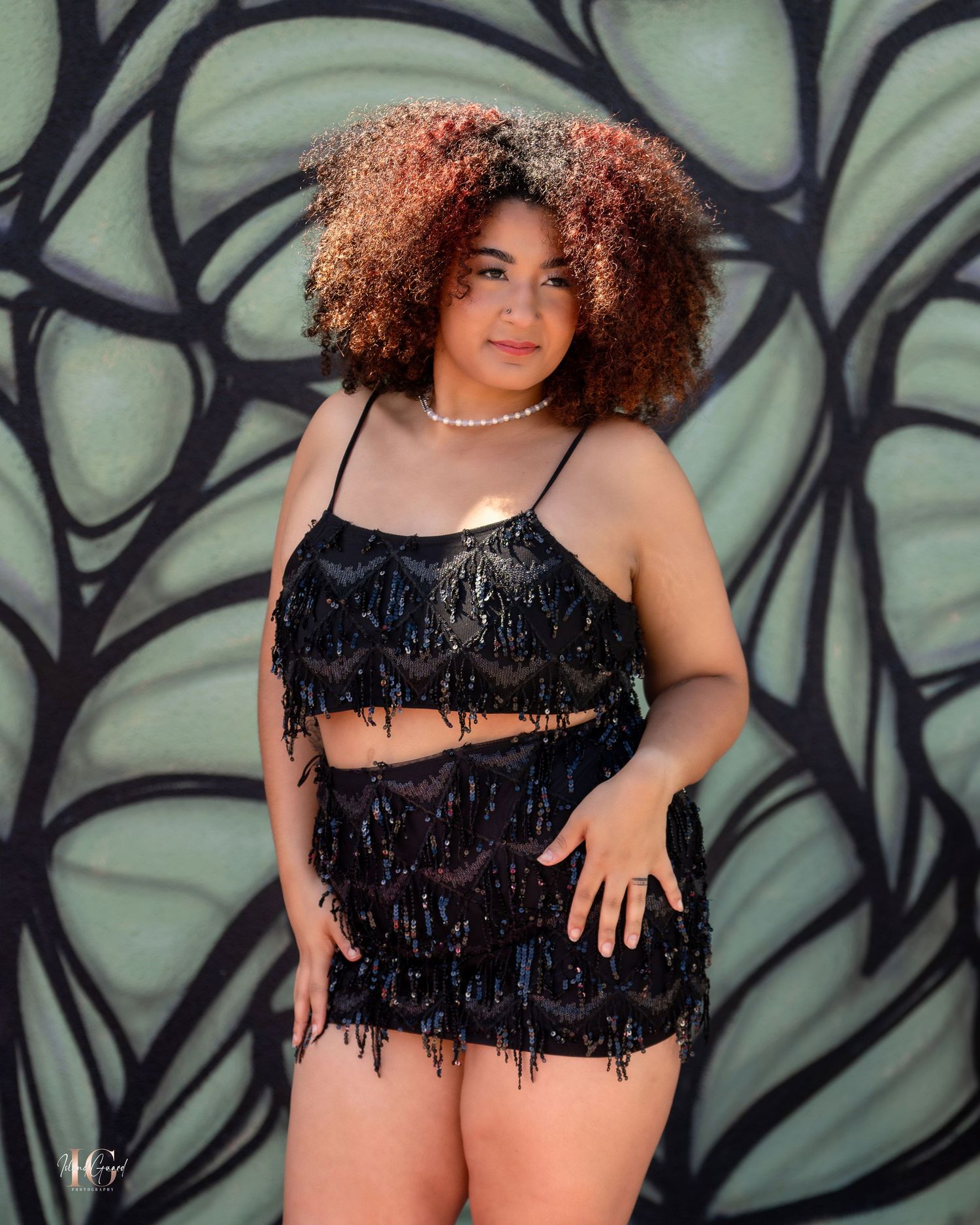 Model in black fringe two-piece outfit poses against geometric wall art.