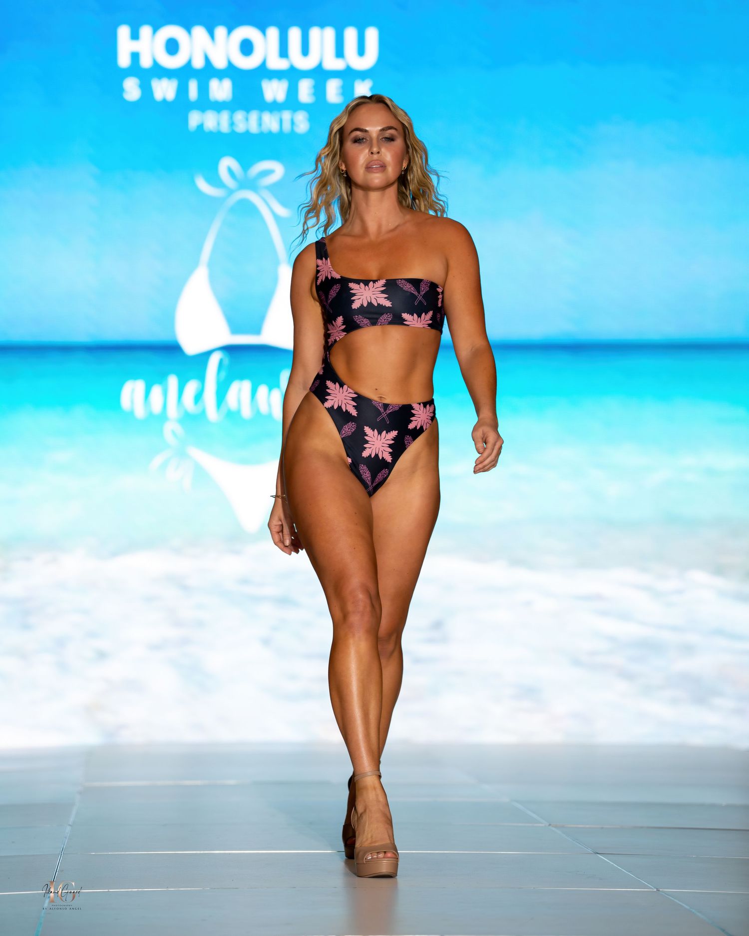 Model showcases floral print bikini on beachwear runway with tropical backdrop.