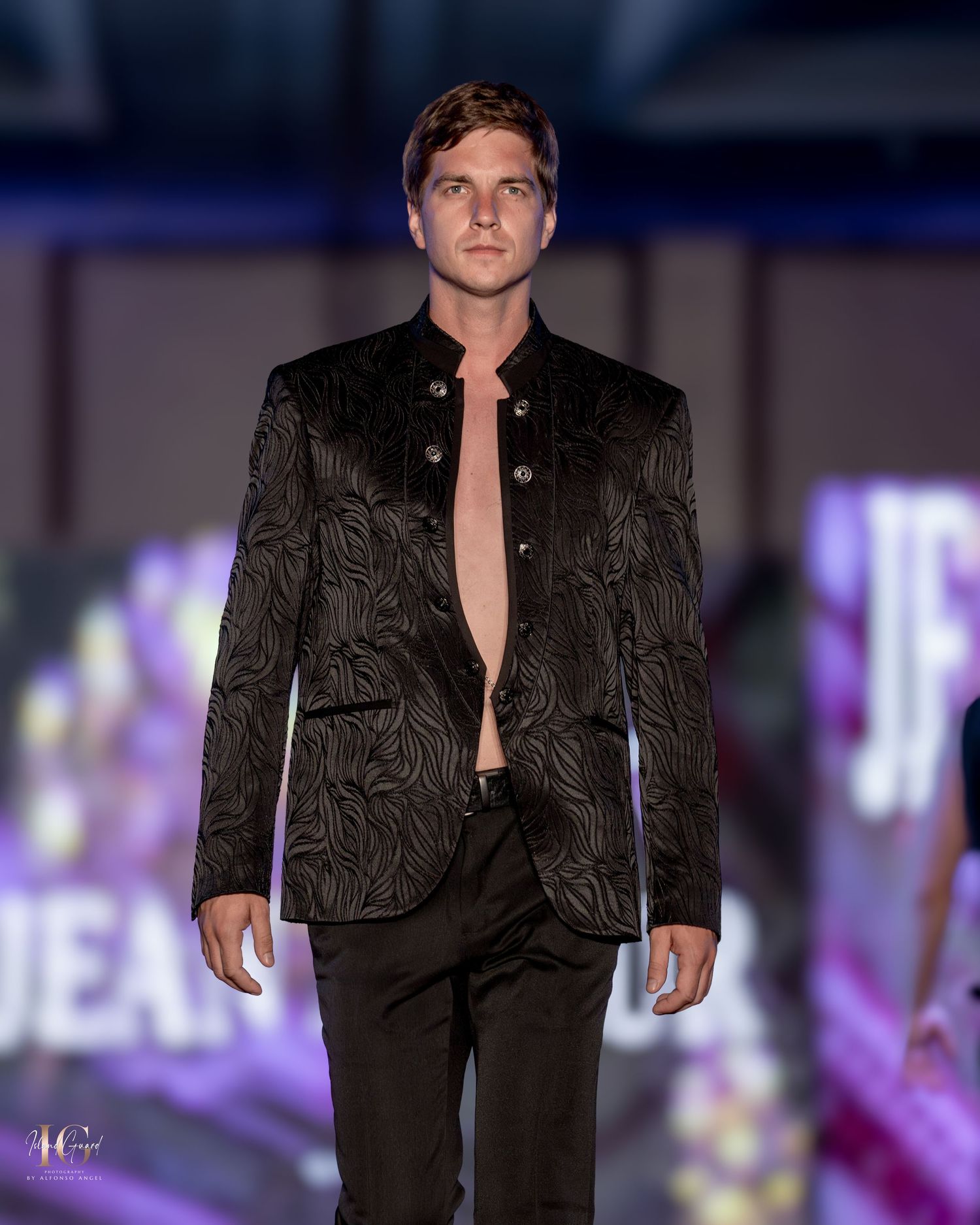 Modern black textured blazer with open chest styling shown on fashion runway.
