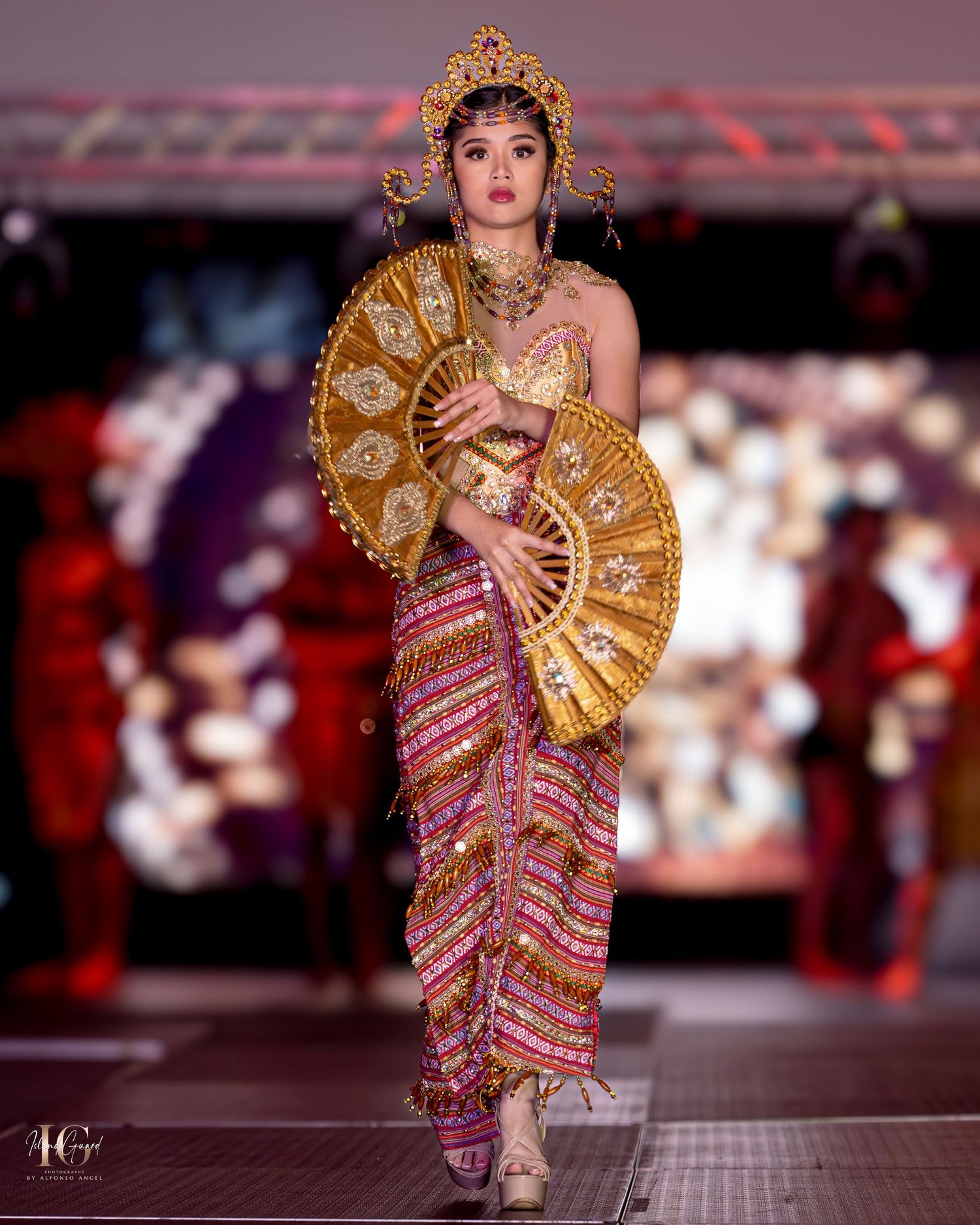 Fashion model in Asian-inspired ensemble with large decorative fan and patterned wrap skirt.