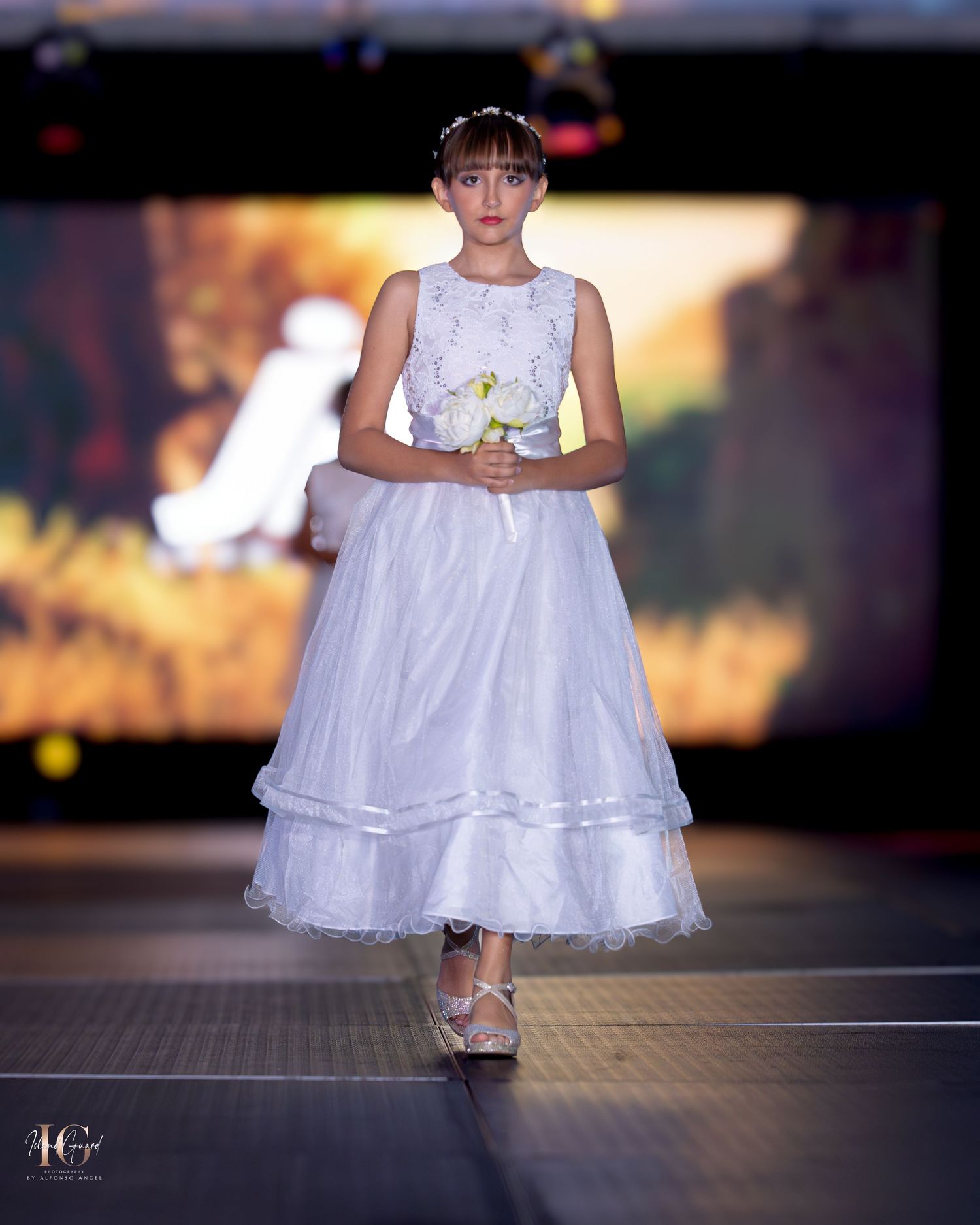 Model wearing white layered tulle dress walks elegantly on fashion runway.