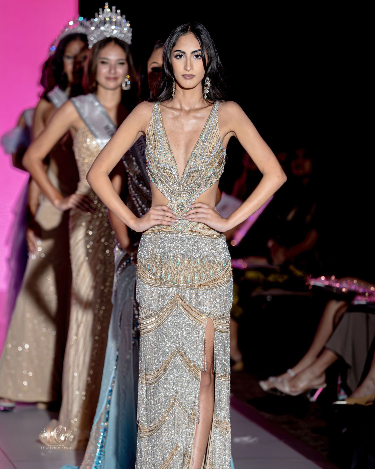 A model walks the runway in a sparkling silver evening gown with geometric beaded patterns and a thigh-high slit.