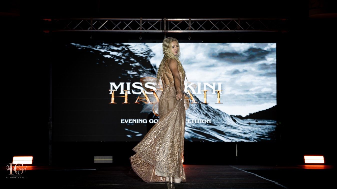 Model wearing a metallic sequin evening gown walks down a fashion runway with dramatic lighting effects.