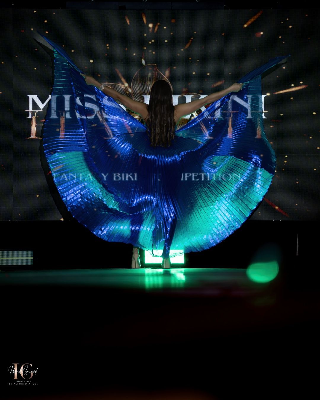 A performer on stage with illuminated blue LED wings stands in dramatic silhouette against a dark background.