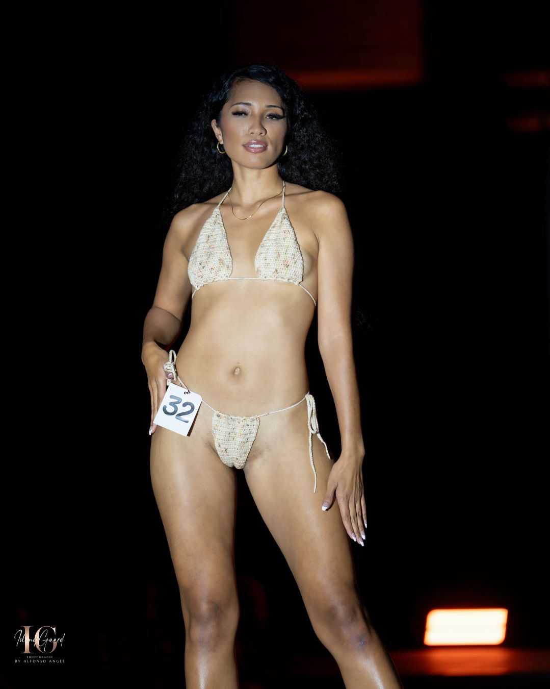 Model showcases white swimwear design on illuminated fashion runway.
