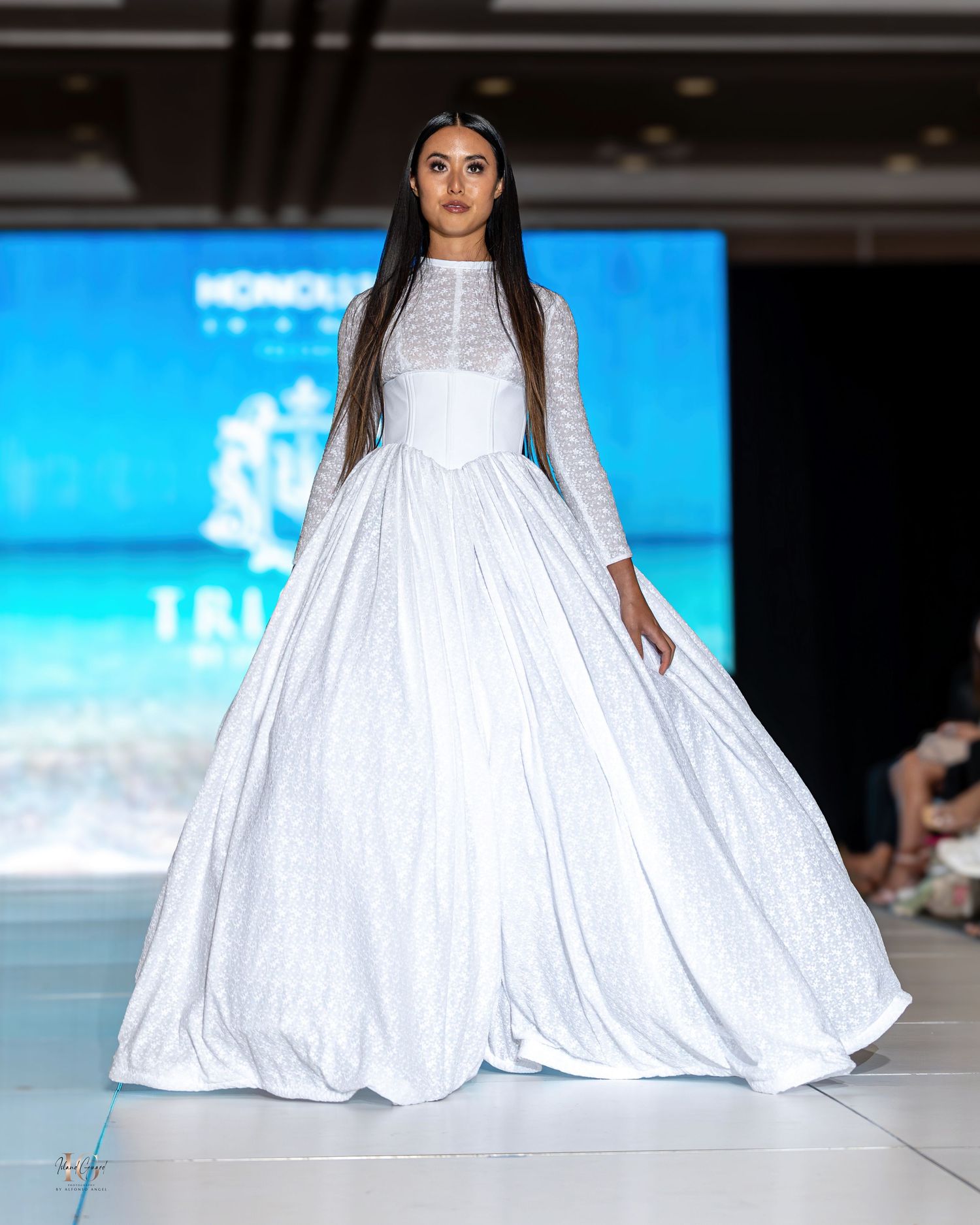 Flowing white maxi dress with dramatic volume showcased on tropical-themed runway.