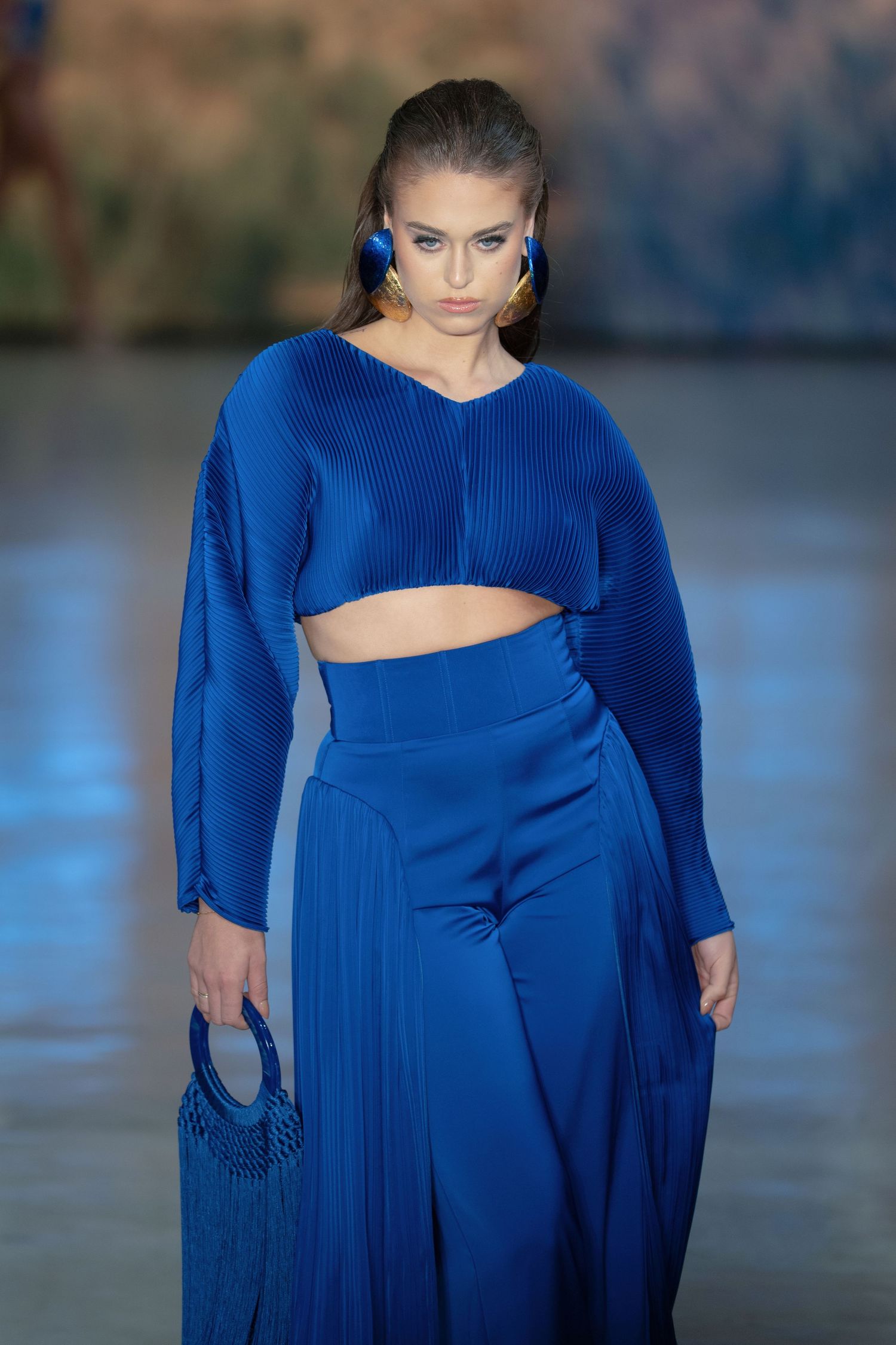 A fashion model walks the runway wearing a vibrant royal blue cutout dress with dramatic draping details.