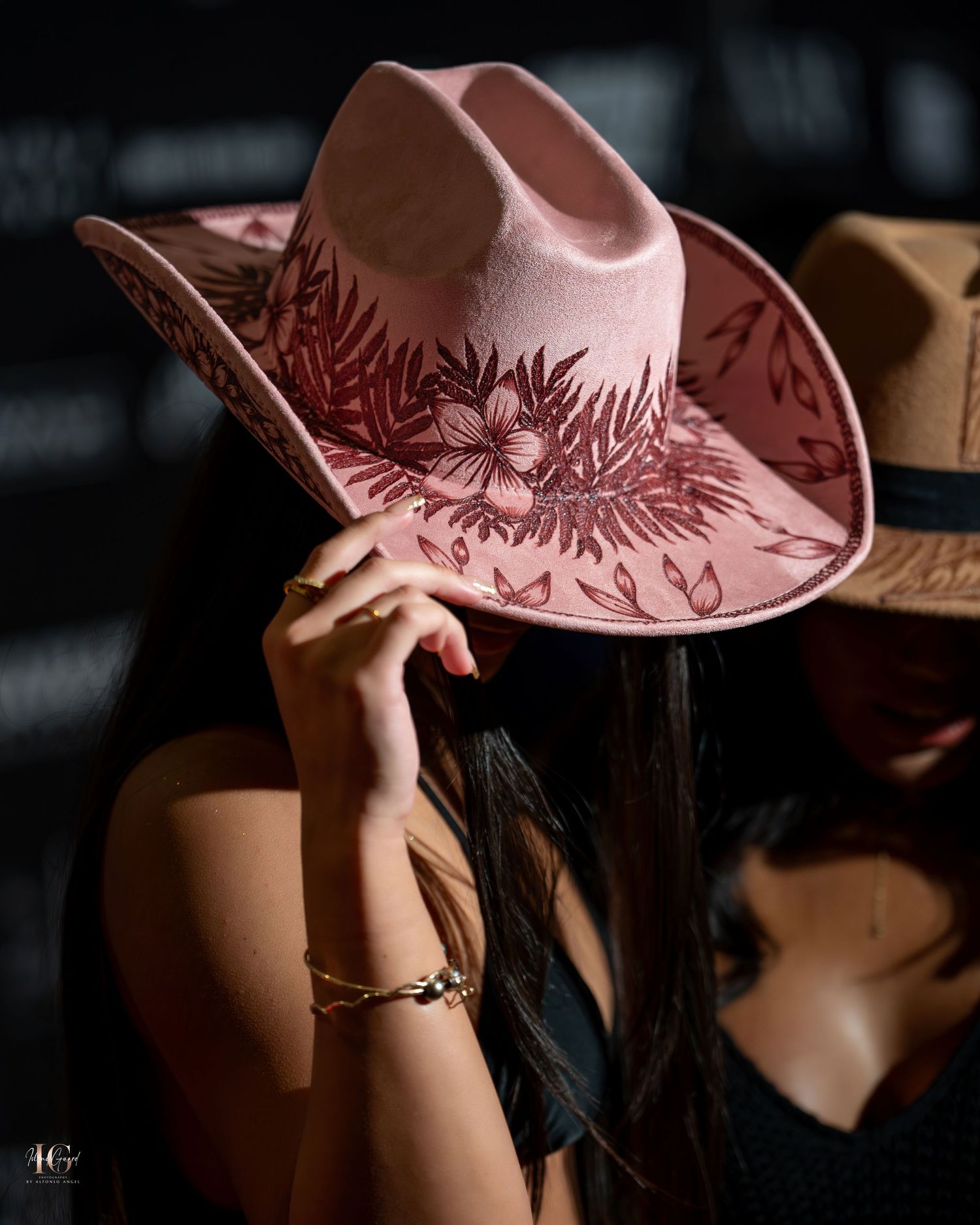 A person wearing a pink cowboy hat with decorative patterns shown from different angles in moody lighting.