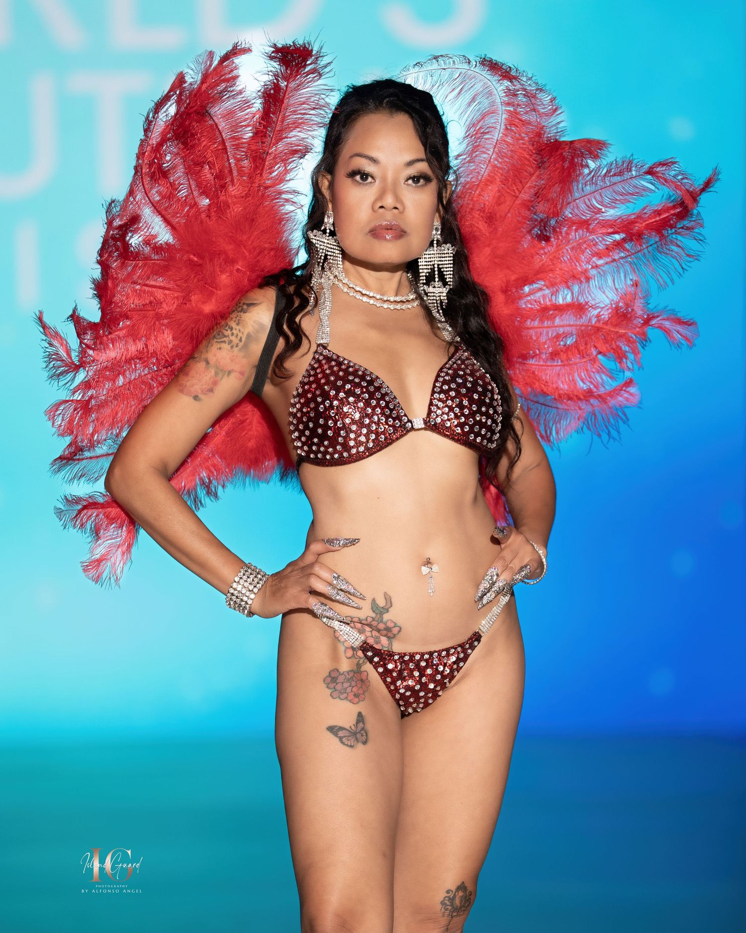 A performer in a polka dot bikini and red feather accessories poses against a blue backdrop.