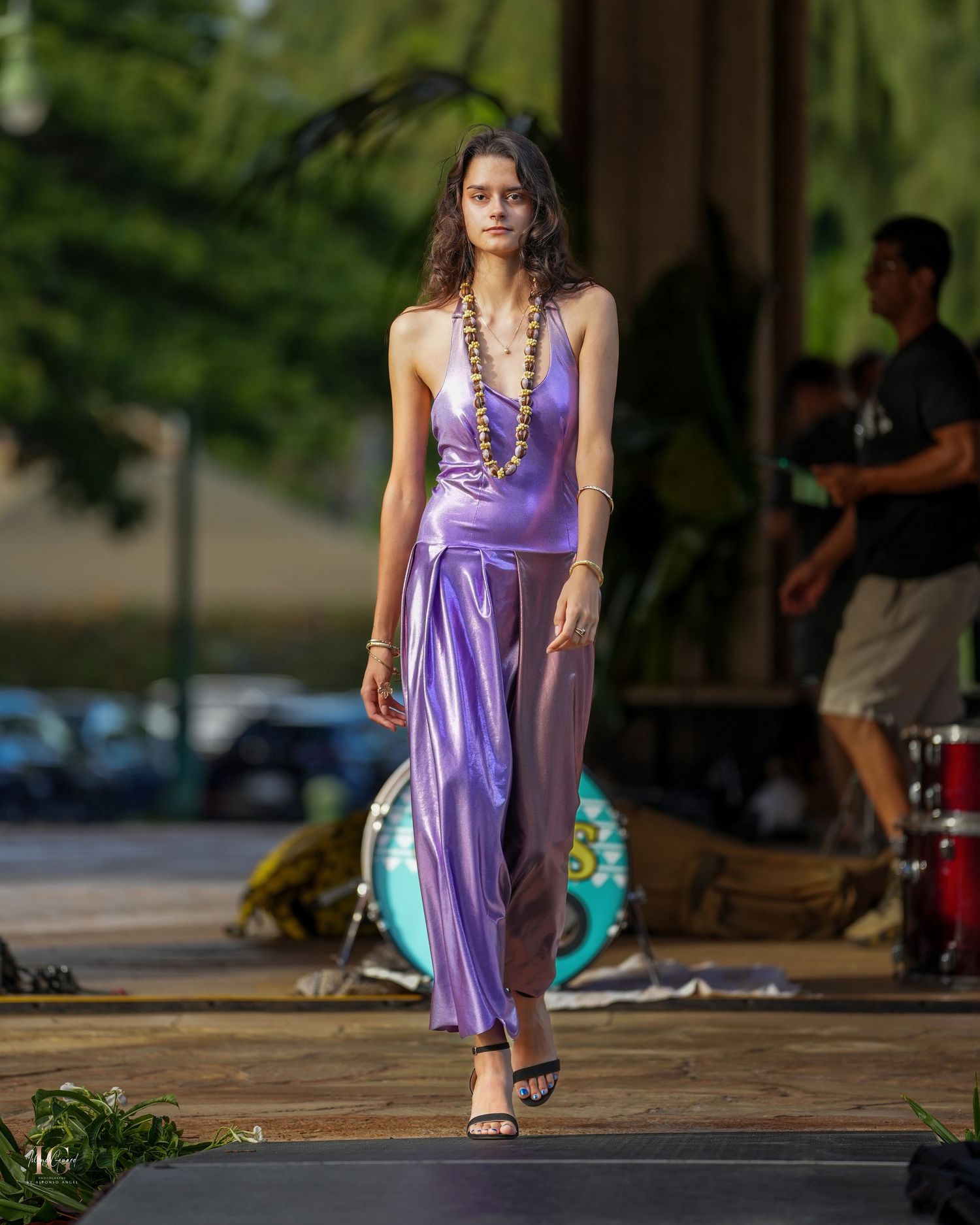 A person in a flowing purple dress walks across a sunlit outdoor patio area.