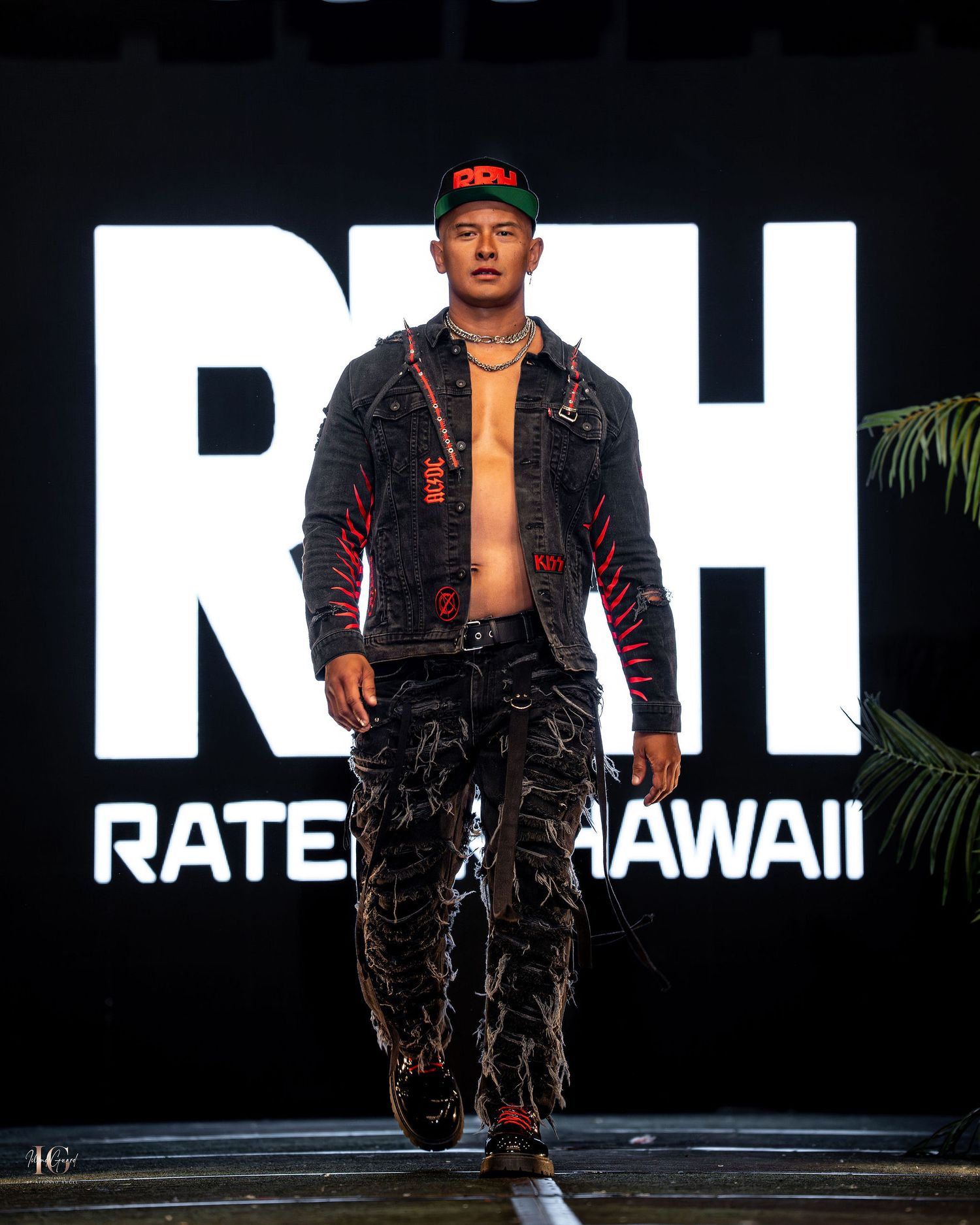 A model walks the runway wearing dark cargo pants and a black jacket against a large white 'RH' backdrop at a fashion show.