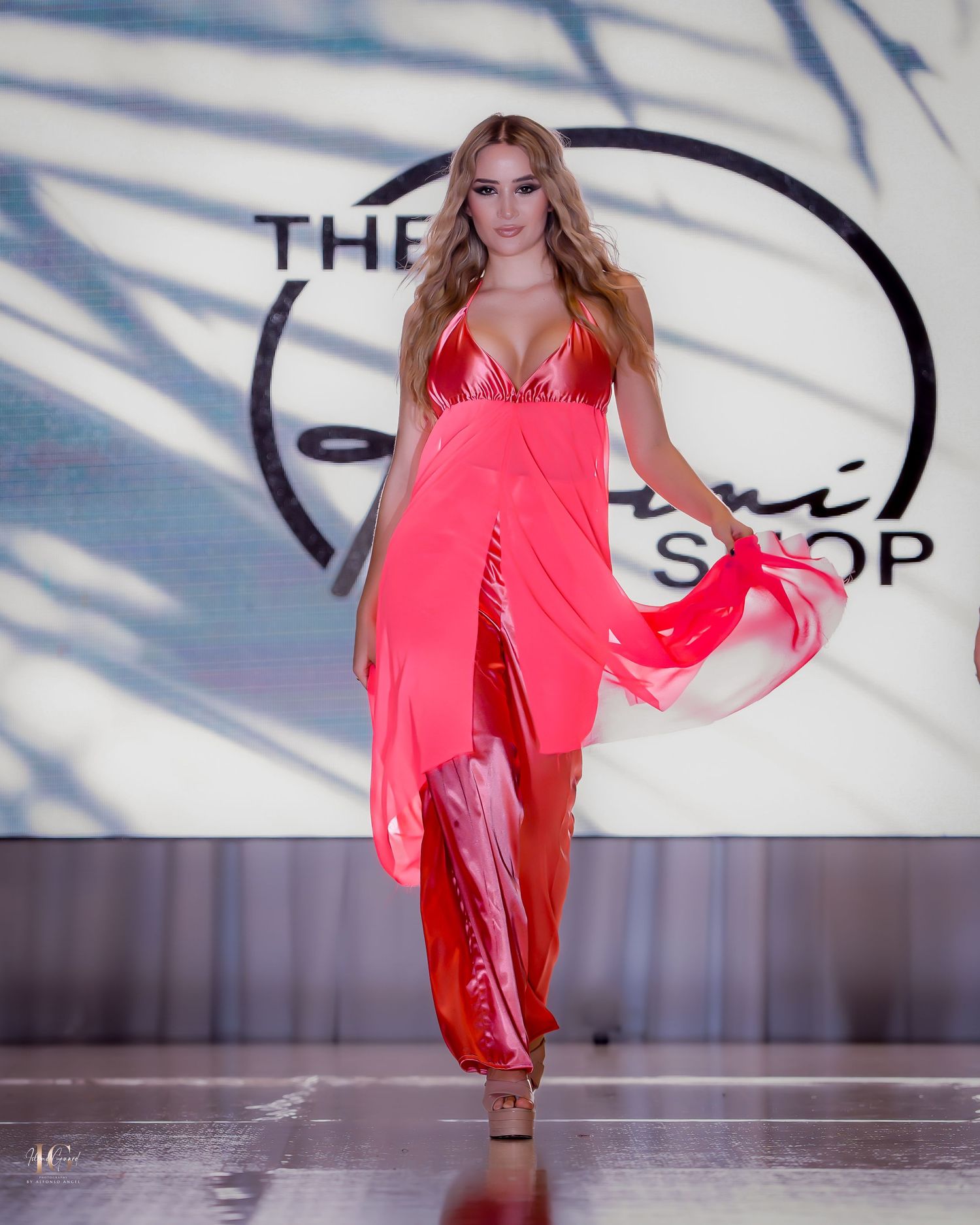 Flowing coral halter dress billows dramatically as model walks fashion runway.