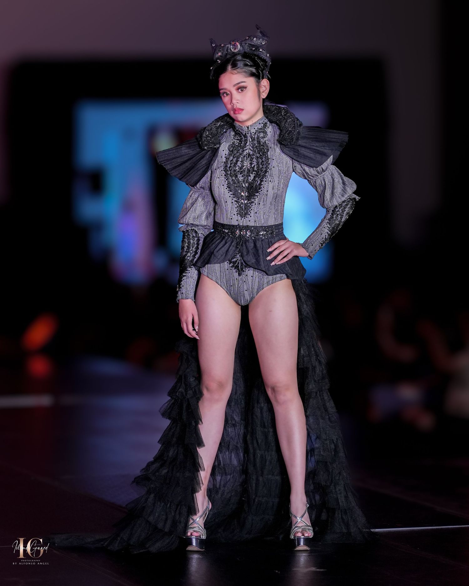 Dramatic black bodysuit with Victorian-inspired neckline and ruffled train shown on fashion runway.