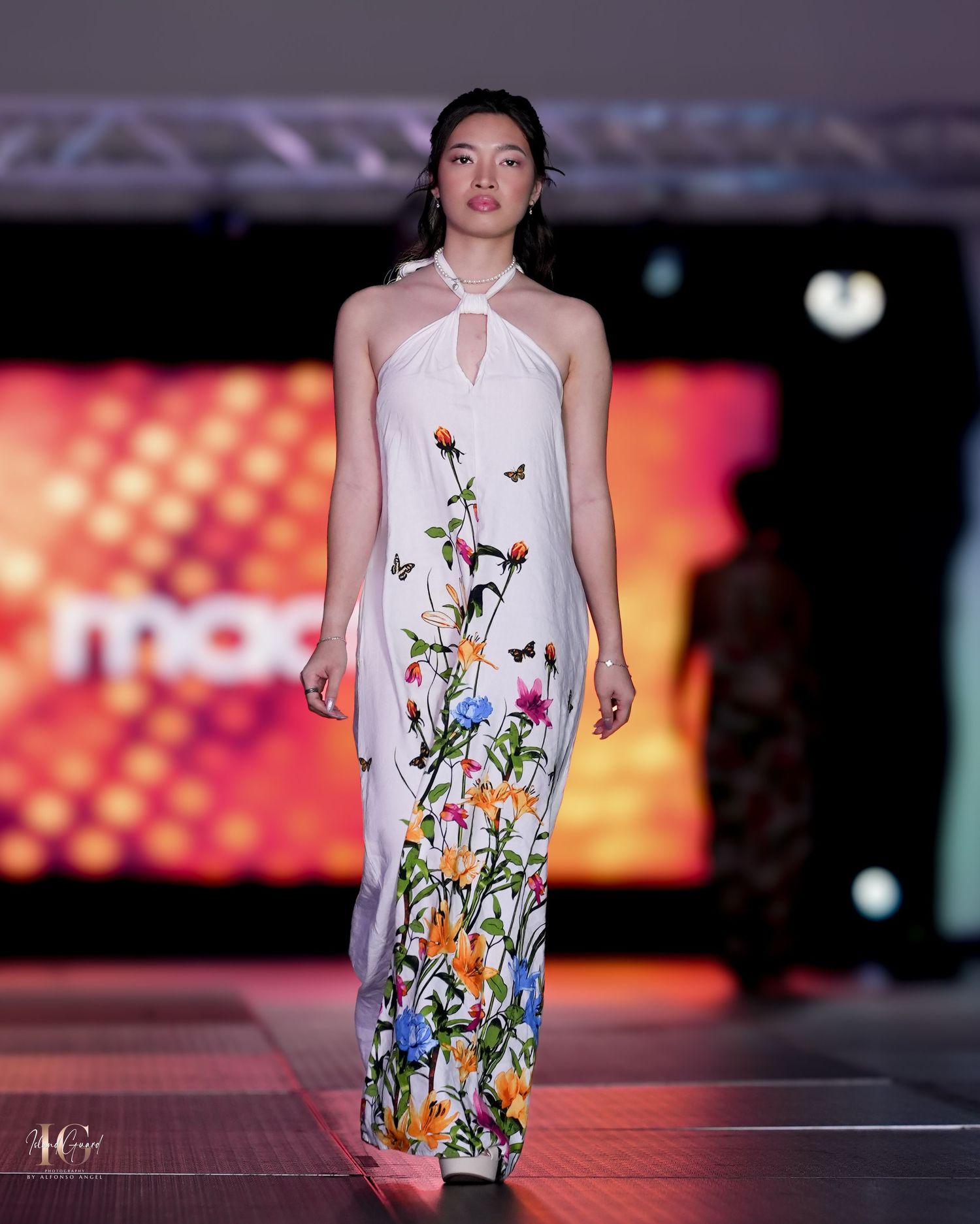 Model walks runway in white halter dress with colorful floral butterfly print along bottom.