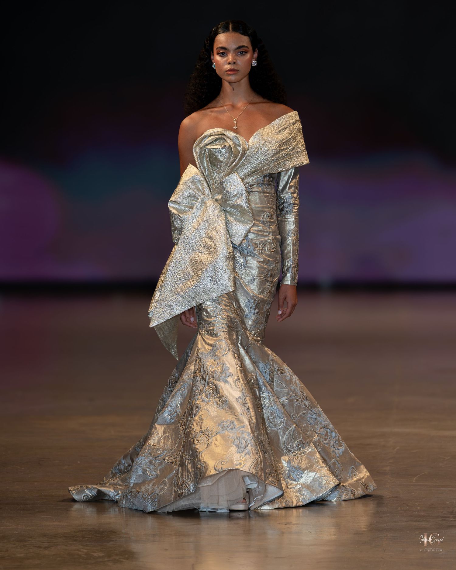 A model walks the runway in a dramatic silver metallic off-shoulder gown with sculptural details at a fashion show.