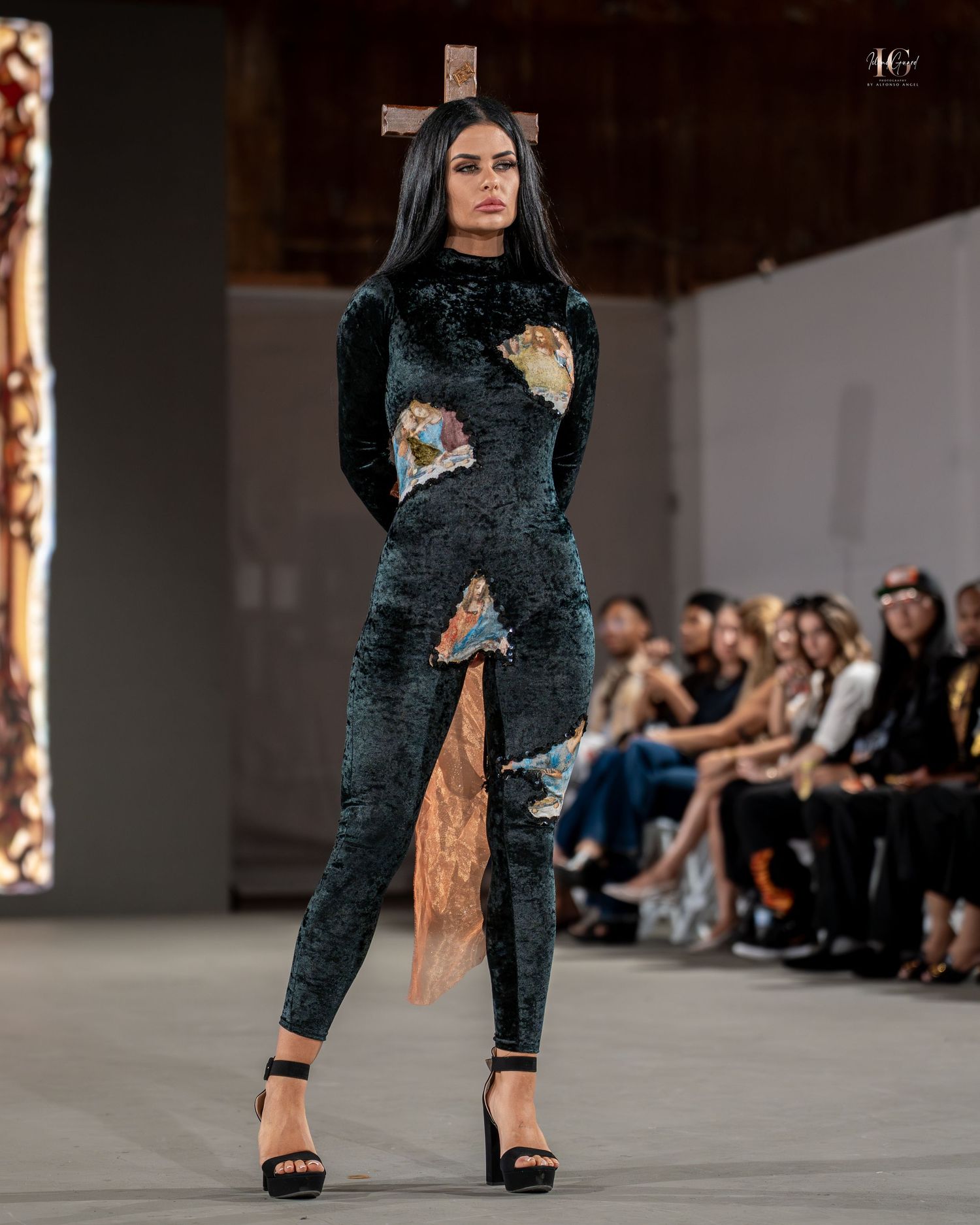 Model walks runway in dark velvet jumpsuit with floral appliques during fashion show.