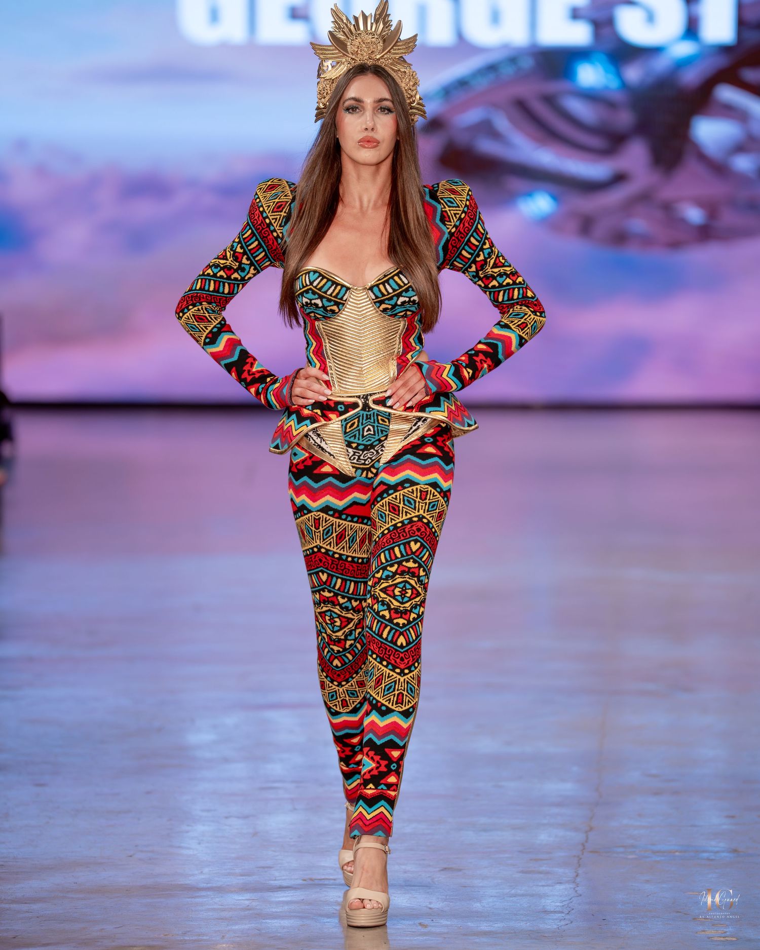 Model walks runway in colorful geometric print bodysuit with long sleeves during fashion show.