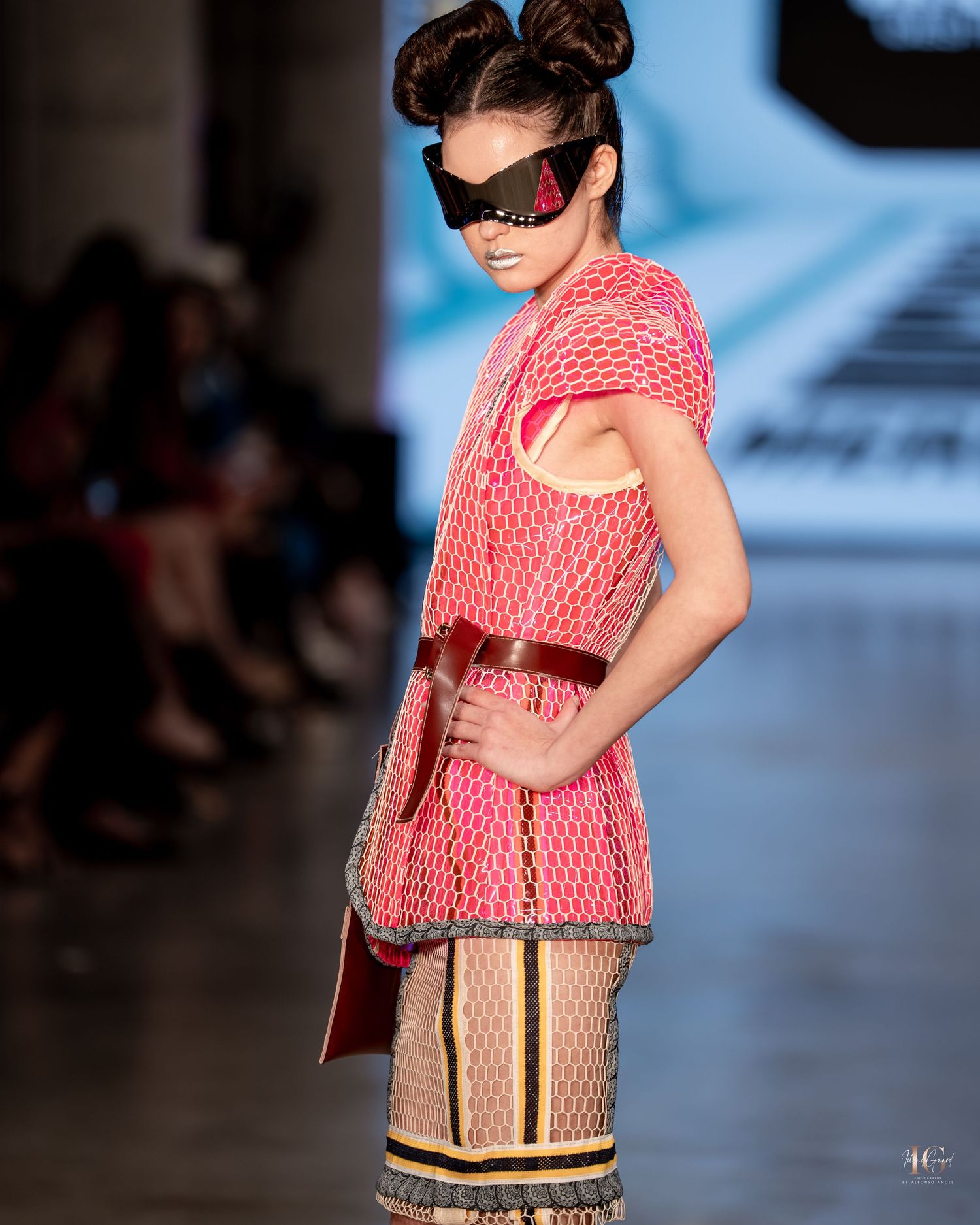 A fashion model walks the runway wearing a coral patterned top and striped skirt at a fashion show.
