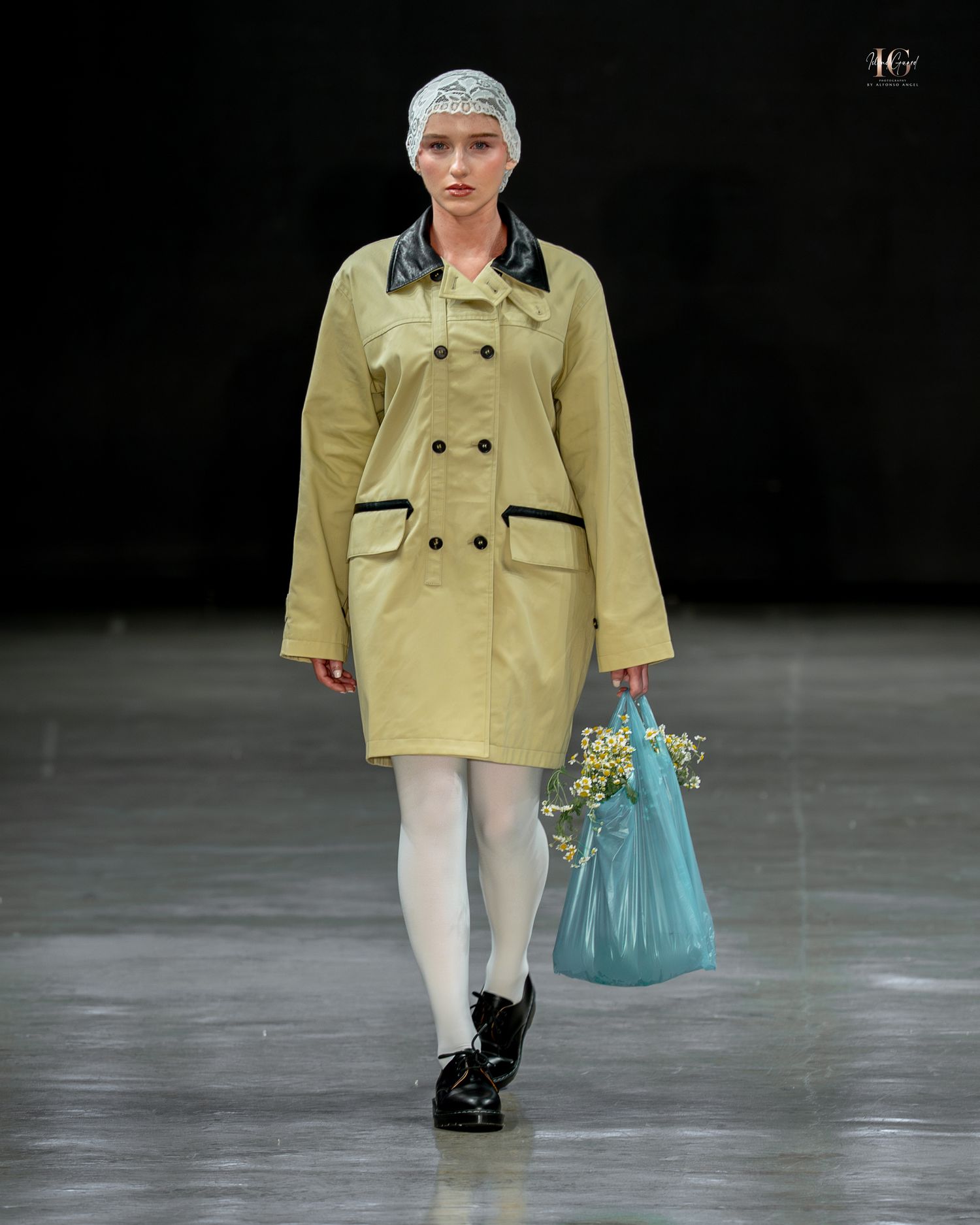 Model walks runway wearing yellow cropped jacket with white pants and turquoise handbag during fashion show.