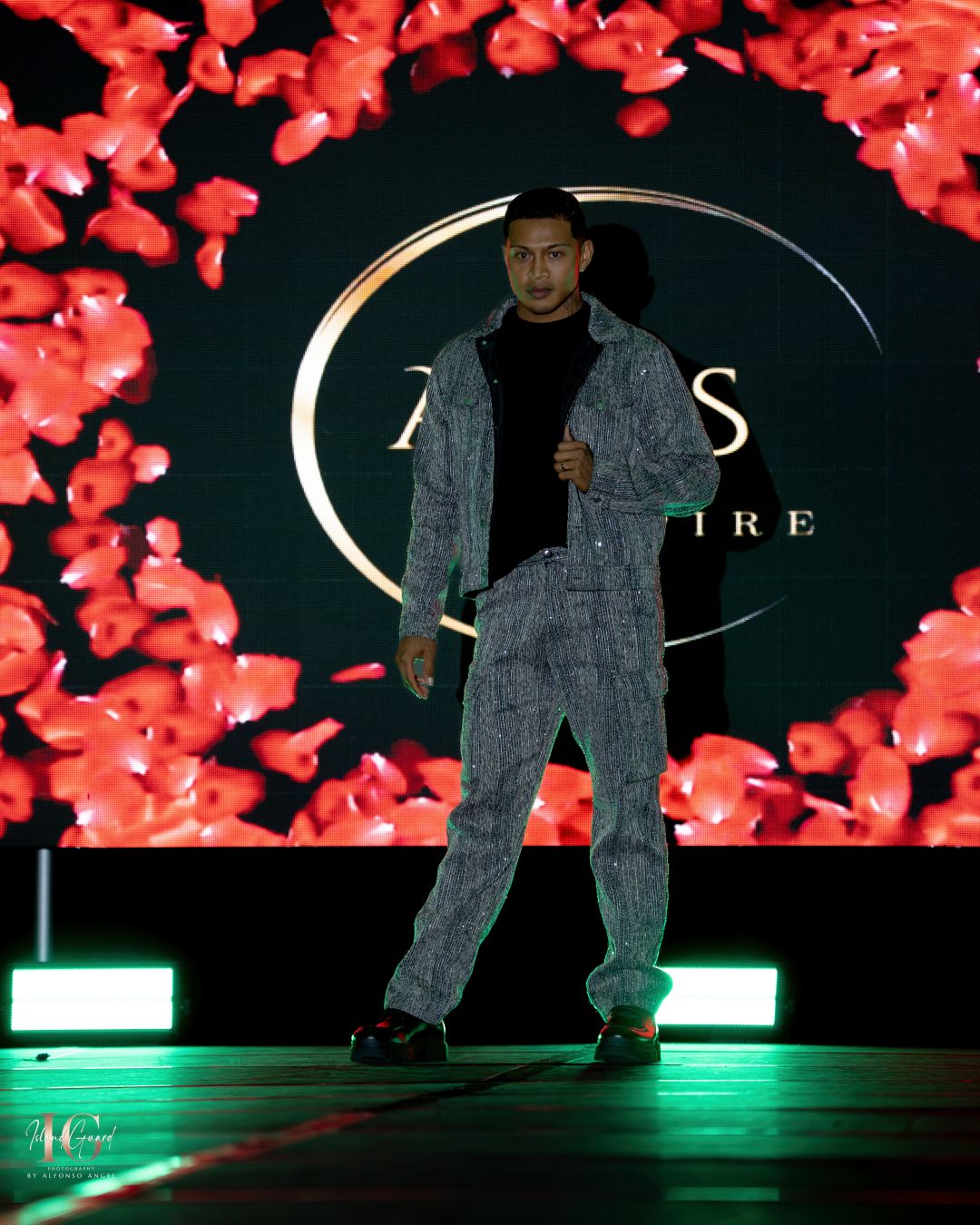 Model showcases grey streetwear outfit with matching jacket and pants on illuminated fashion runway.