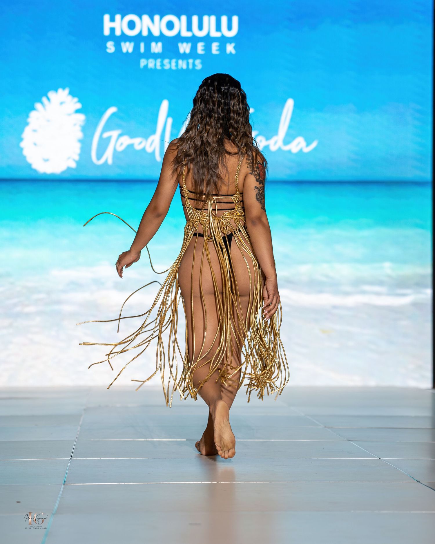 Beachwear collection featuring tan fringed swimsuit against ocean backdrop at Honolulu fashion show.