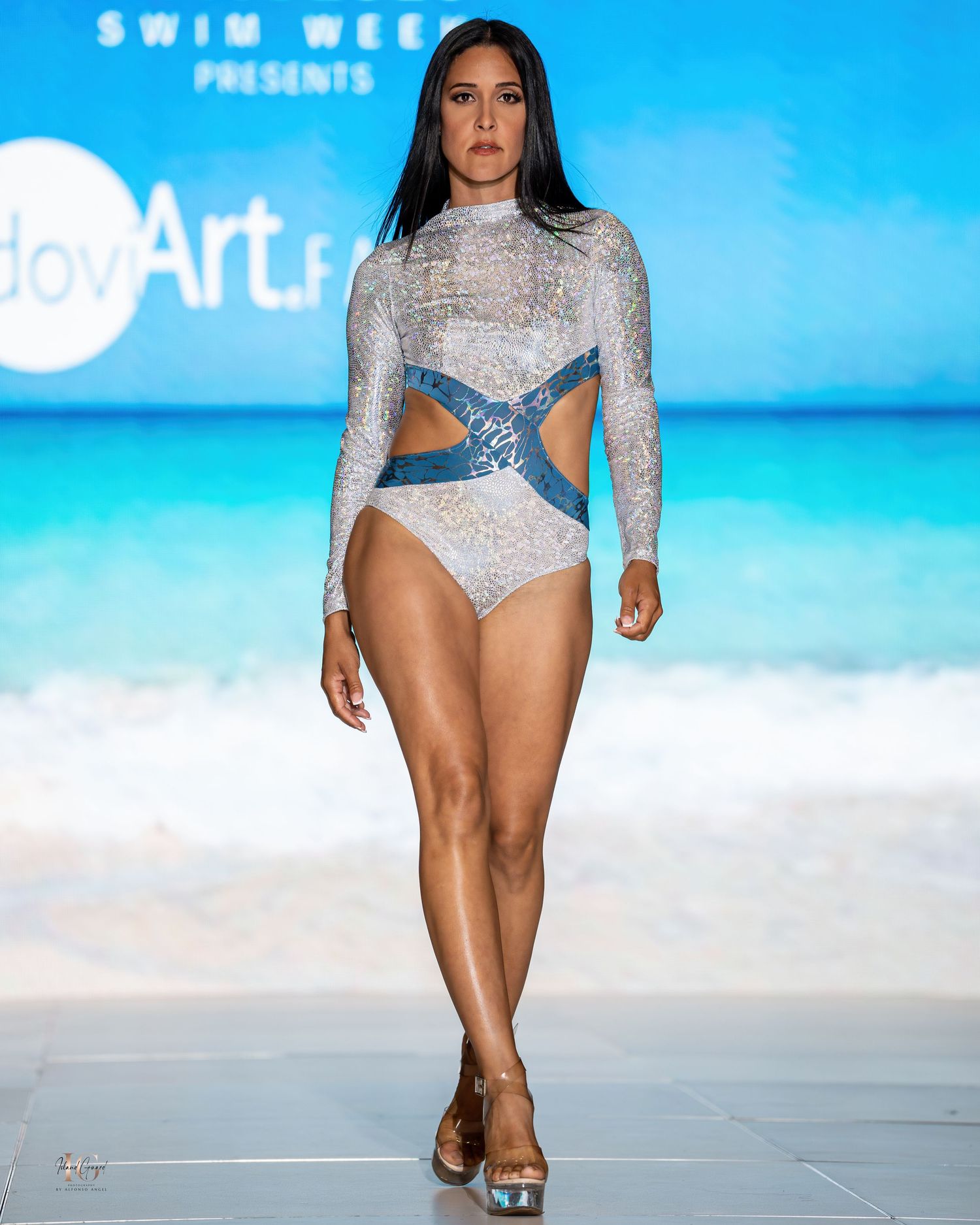 Model walks runway in sparkly silver swimwear with long sleeves during Honolulu Swim Week fashion show.
