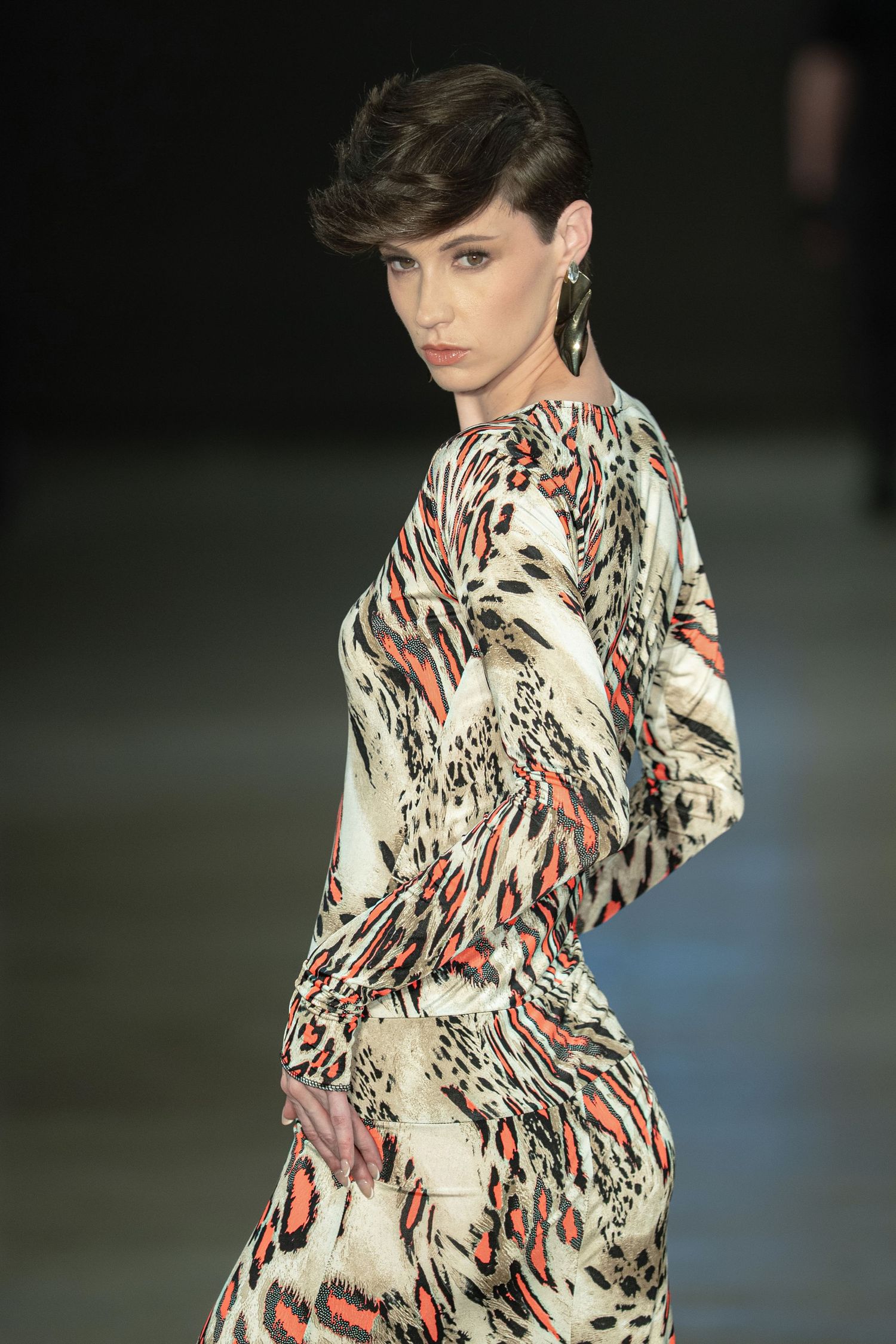 Model wearing a long-sleeved dress with abstract animal print pattern in beige and red tones on the runway.