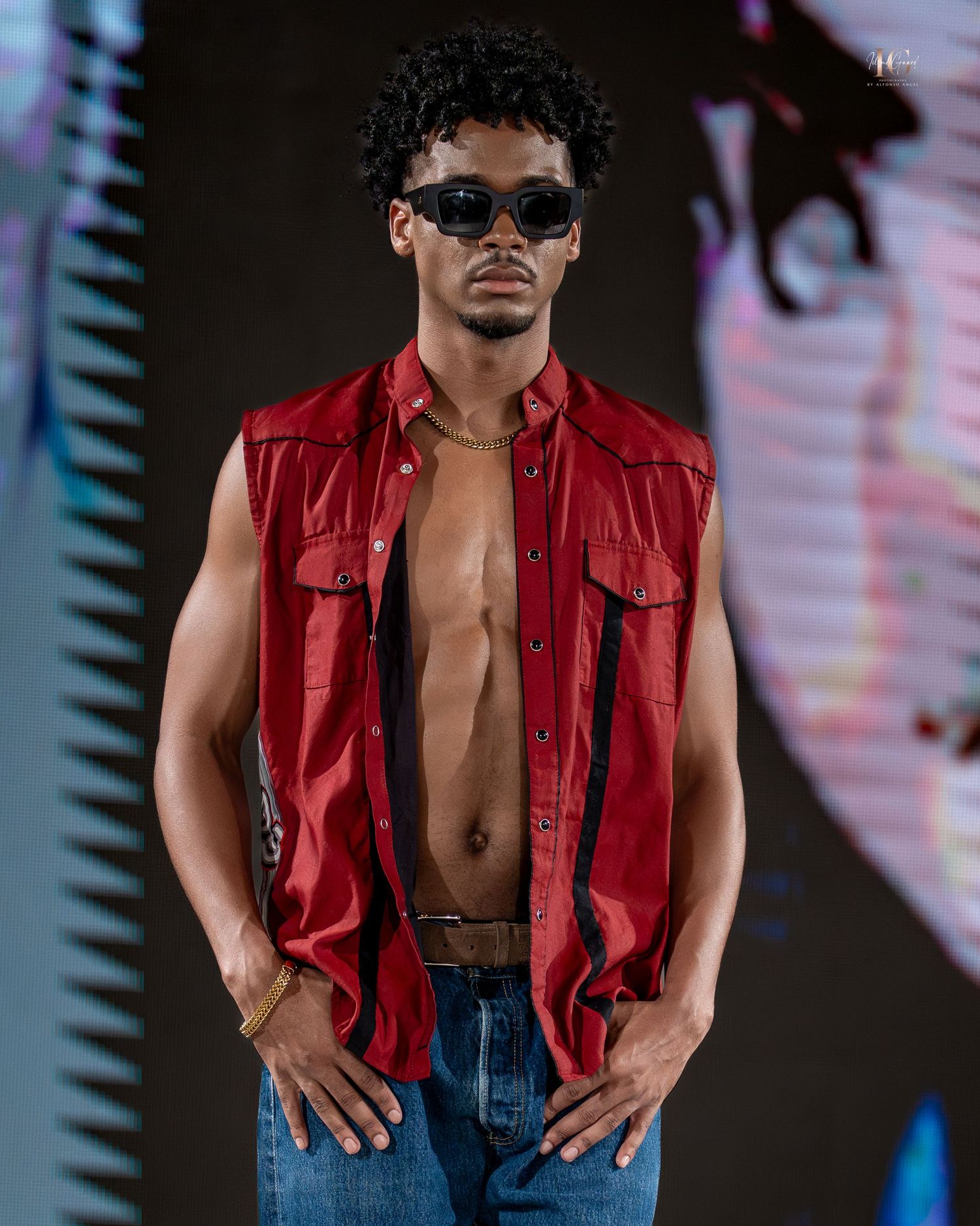 Person in sunglasses and red leather vest poses confidently against dark background with neon lighting effects.