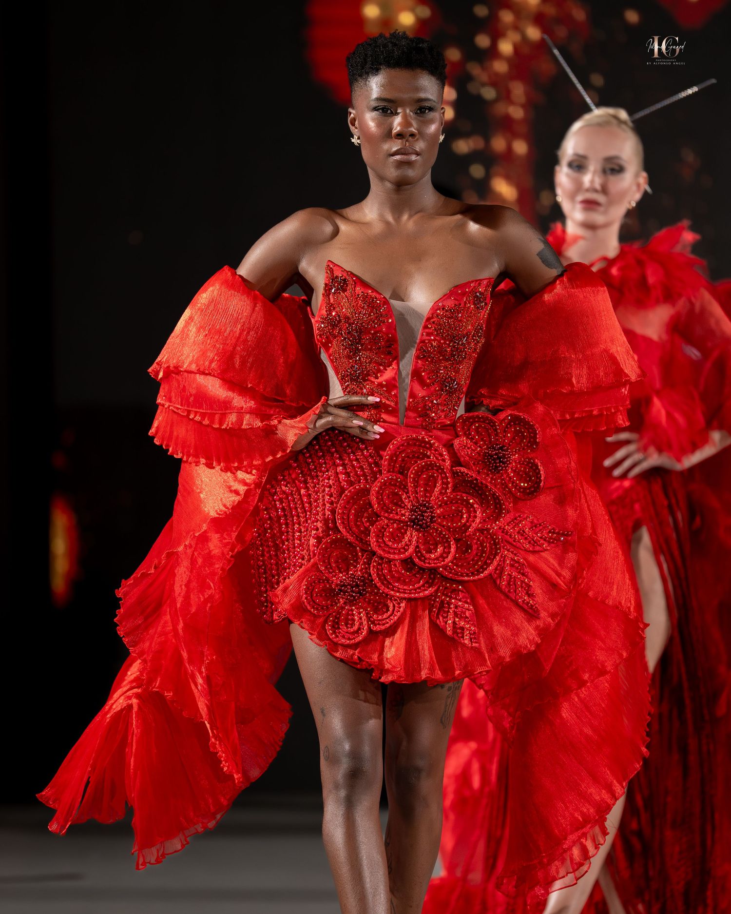 Models walk the runway in dramatic red ruffled couture gowns with sculptural details at a fashion show.