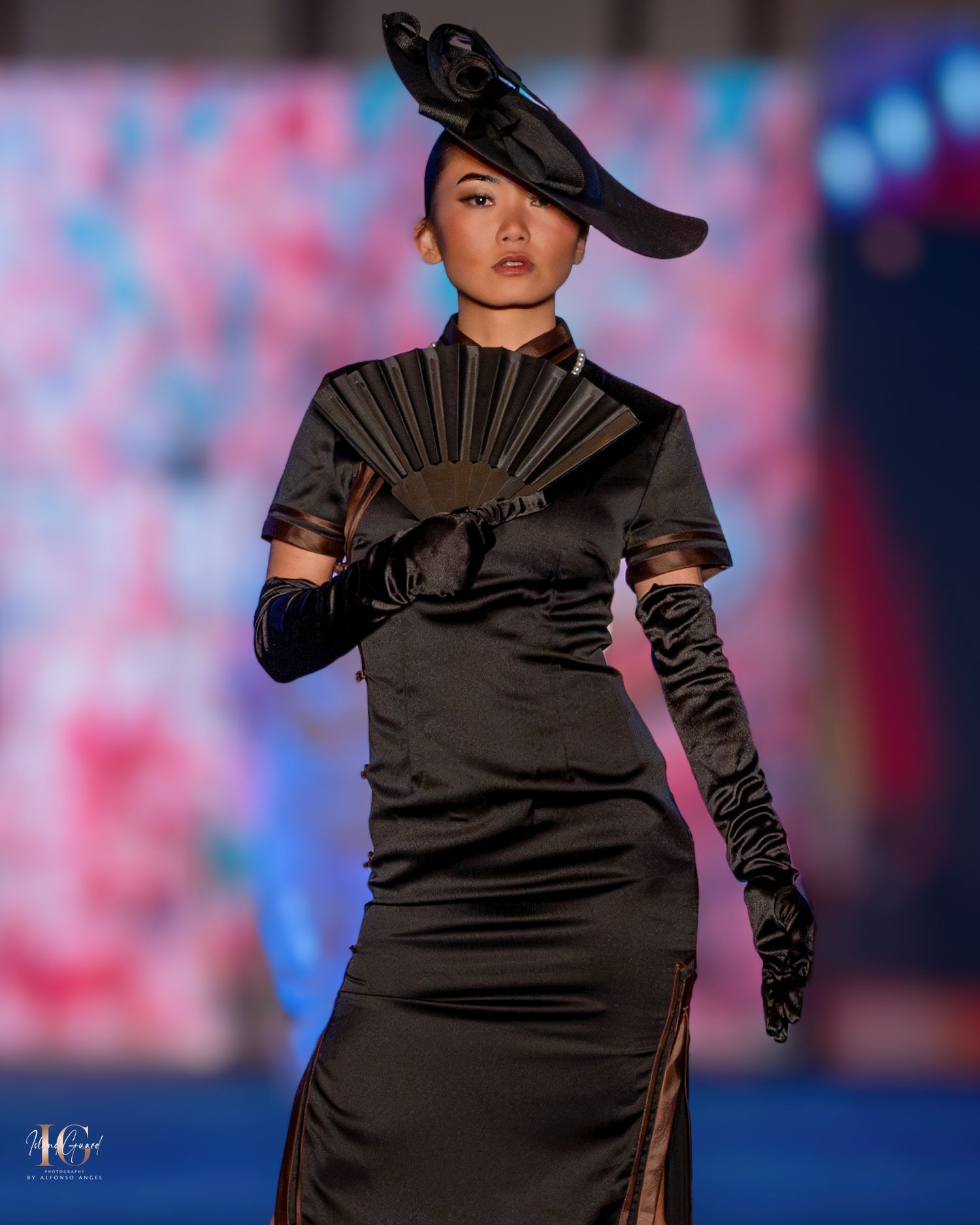 Sleek black evening gown with matching gloves and hat presented at fashion show.