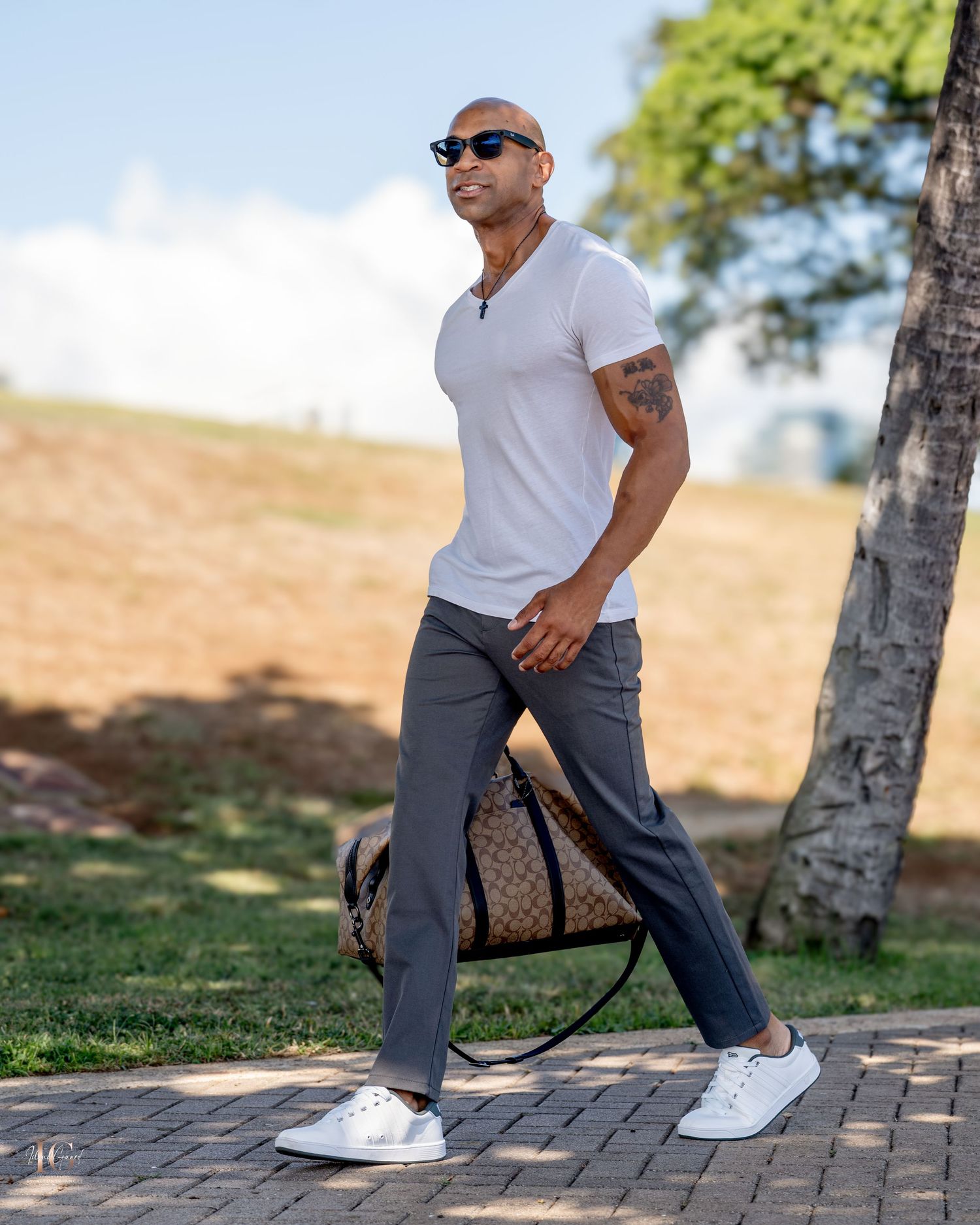 Person in sunglasses and white t-shirt strikes casual poses against tree backdrop in outdoor setting.