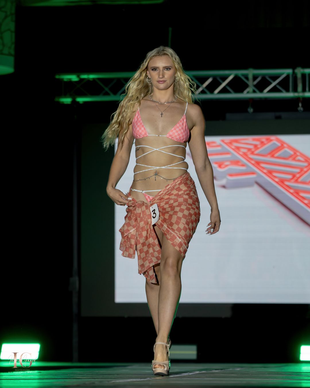 Model showcases pink and orange beachwear ensemble while walking fashion runway.