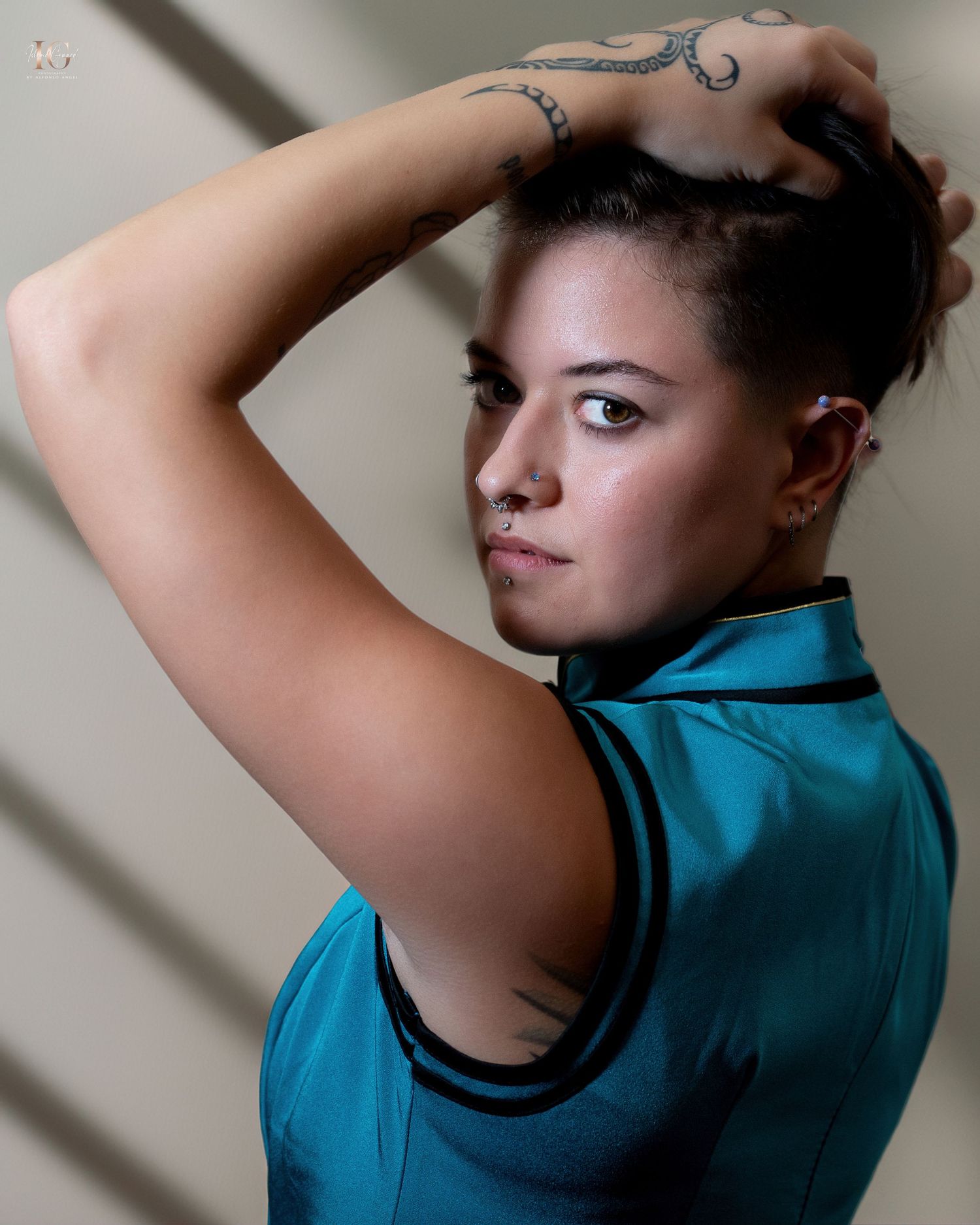 Portrait shot in soft light shows an athletic figure in a vibrant turquoise sleeveless top with dramatic shadows and a tattoo.