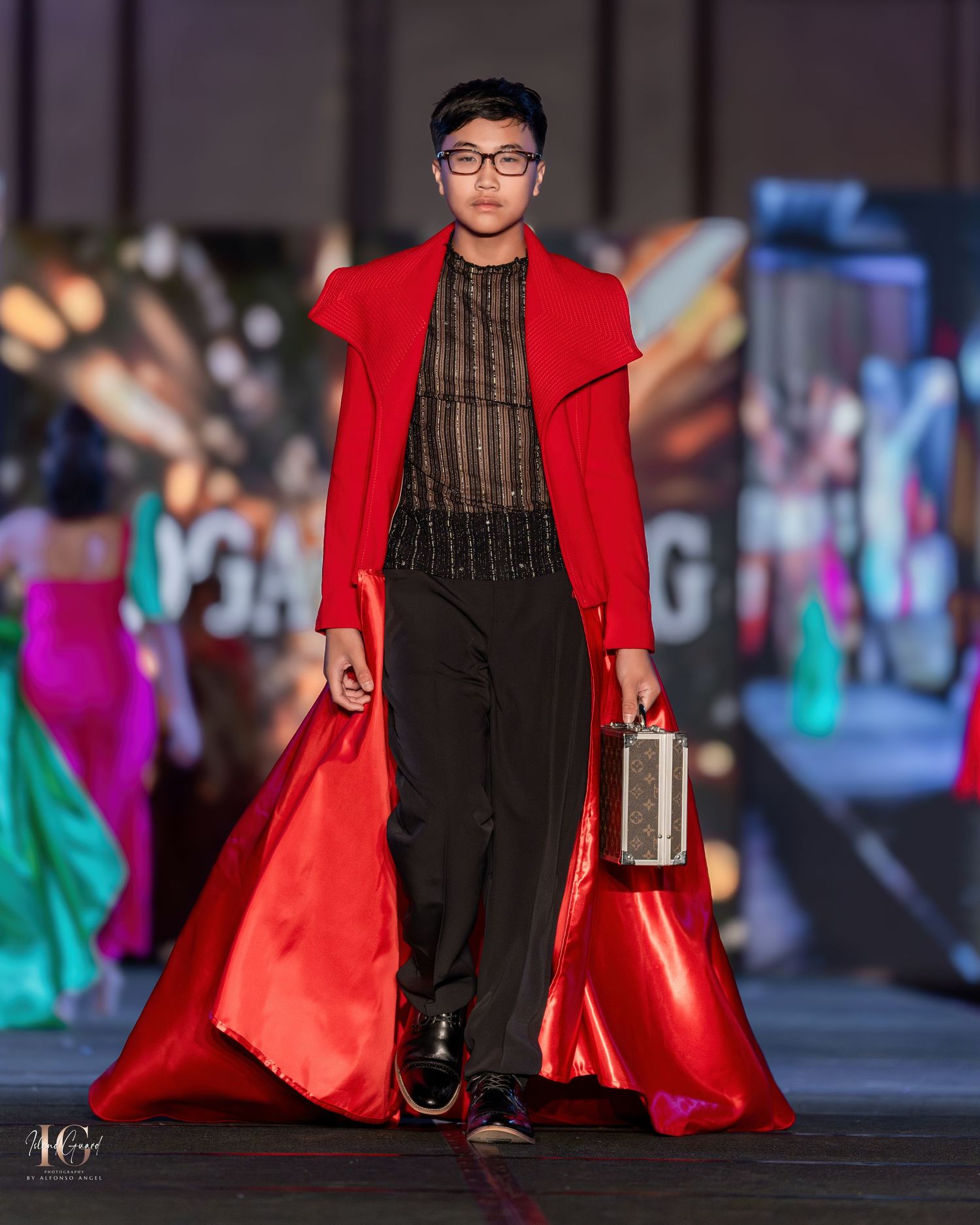 Model wearing black mesh top with striking red coat walking runway fashion show.