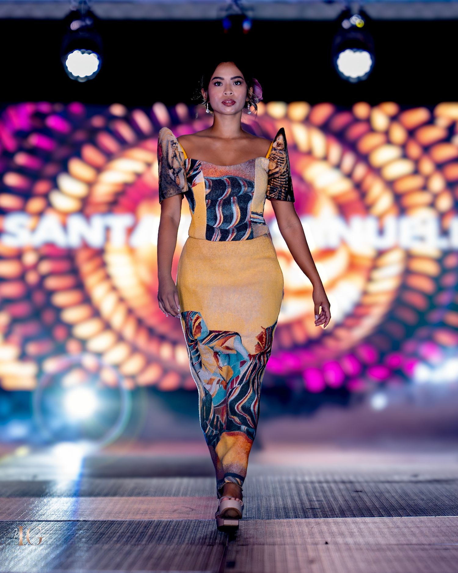 Elegant fitted dress featuring mustard yellow and blue pattern design displayed on illuminated catwalk.