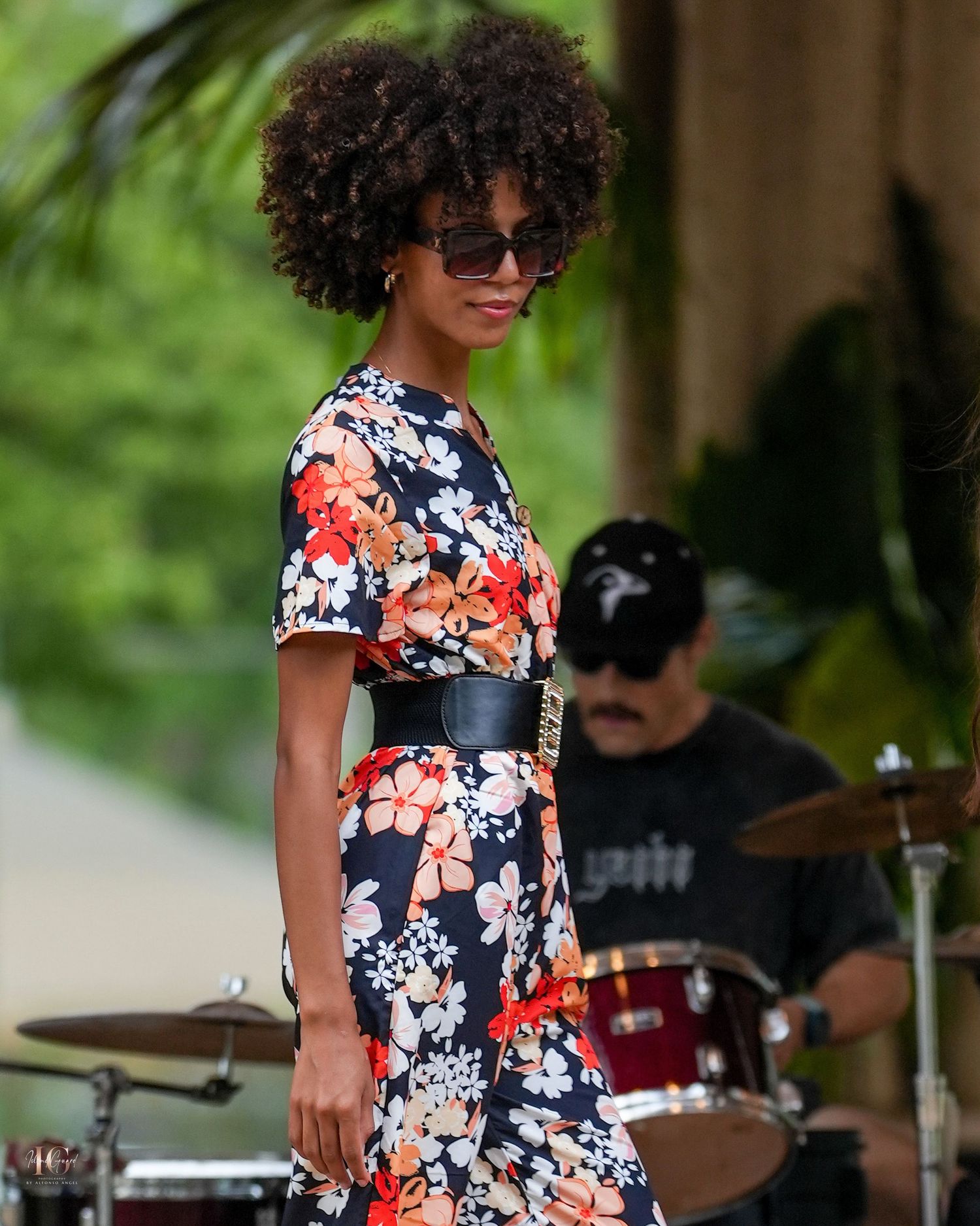 Singer performs in a vibrant floral dress at an outdoor concert with a band playing in the background.