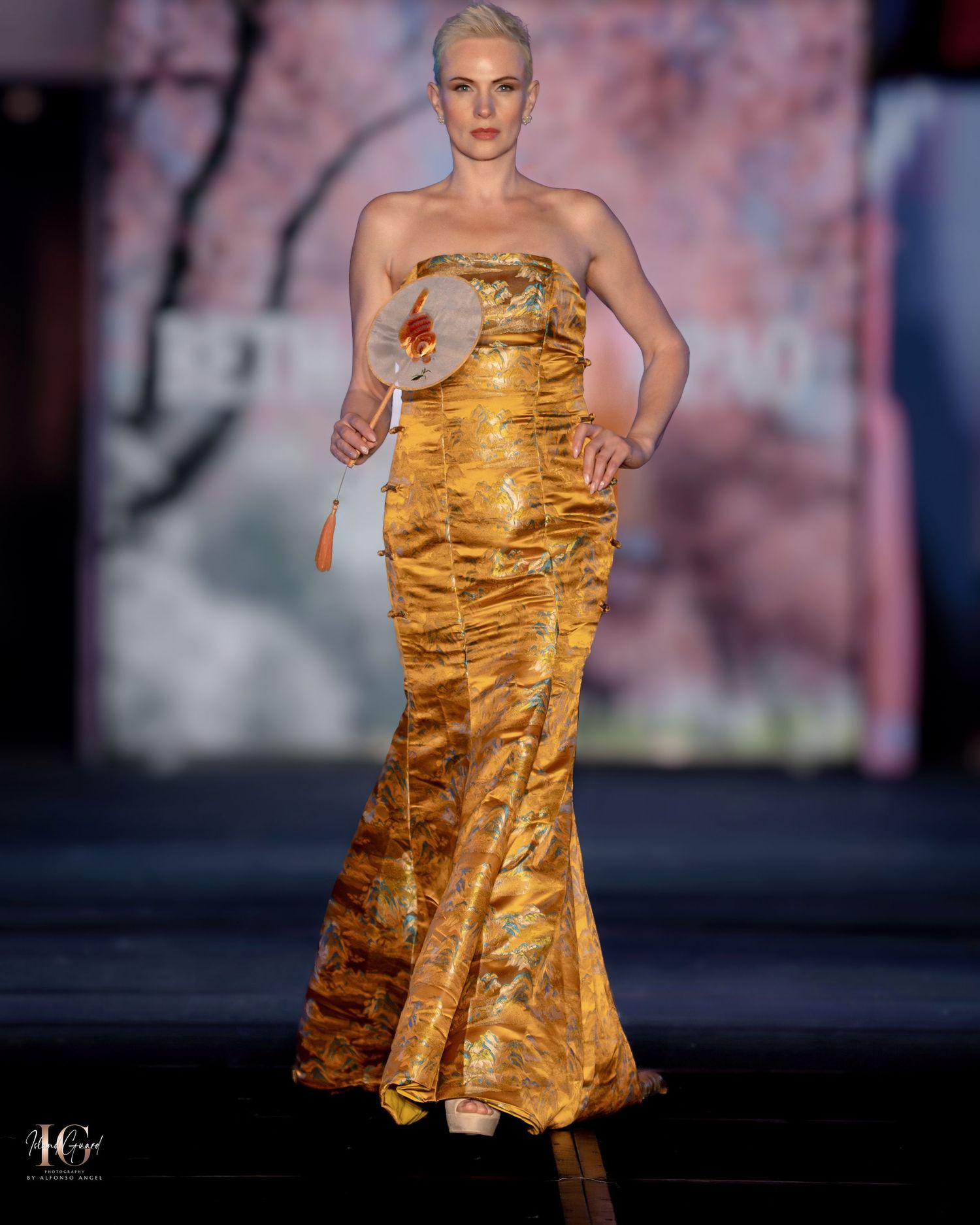 Strapless gold mermaid gown with ruched details shown on fashion runway.