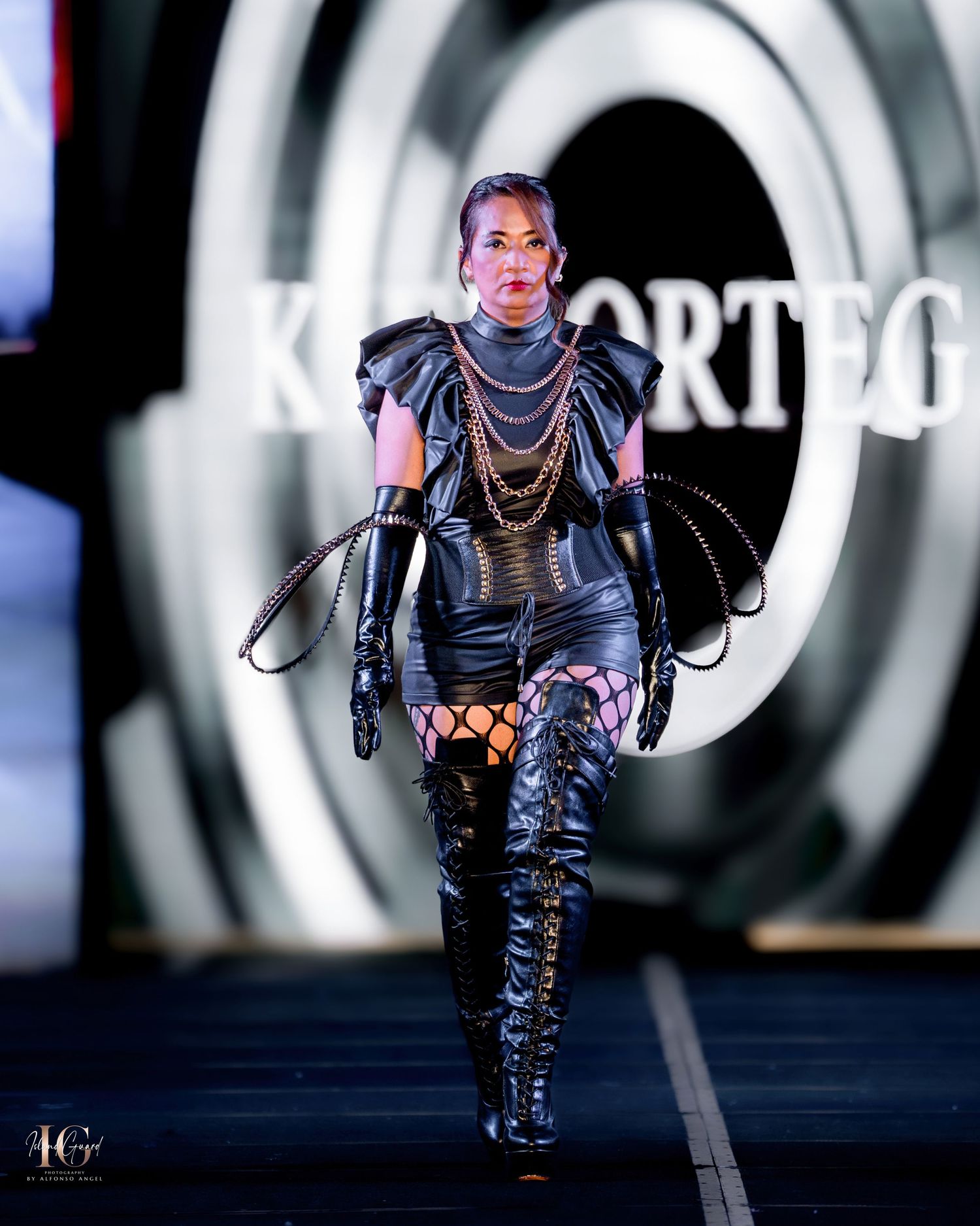 Model showcases futuristic black armor-inspired outfit with chain details and thigh-high boots.