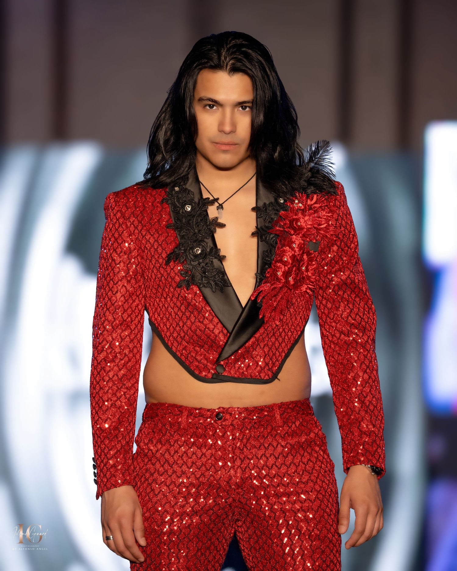 Red sequined suit ensemble on model strutting down fashion runway with theatrical background.
