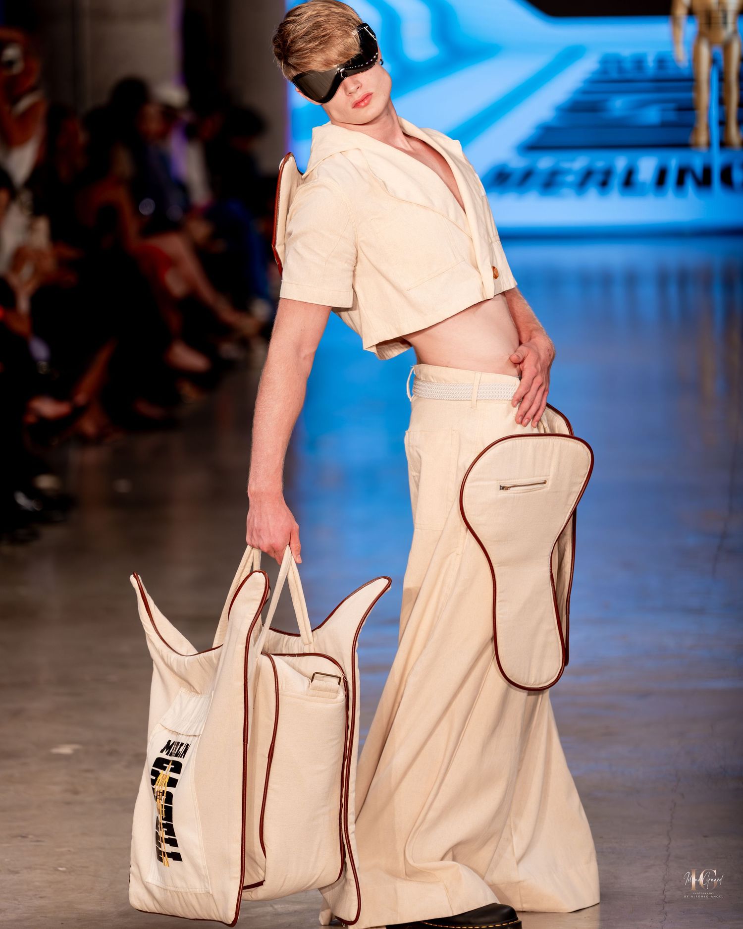 Fashion model walks runway wearing beige utility-inspired dress with contrasting piping and matching handbag at fashion show.