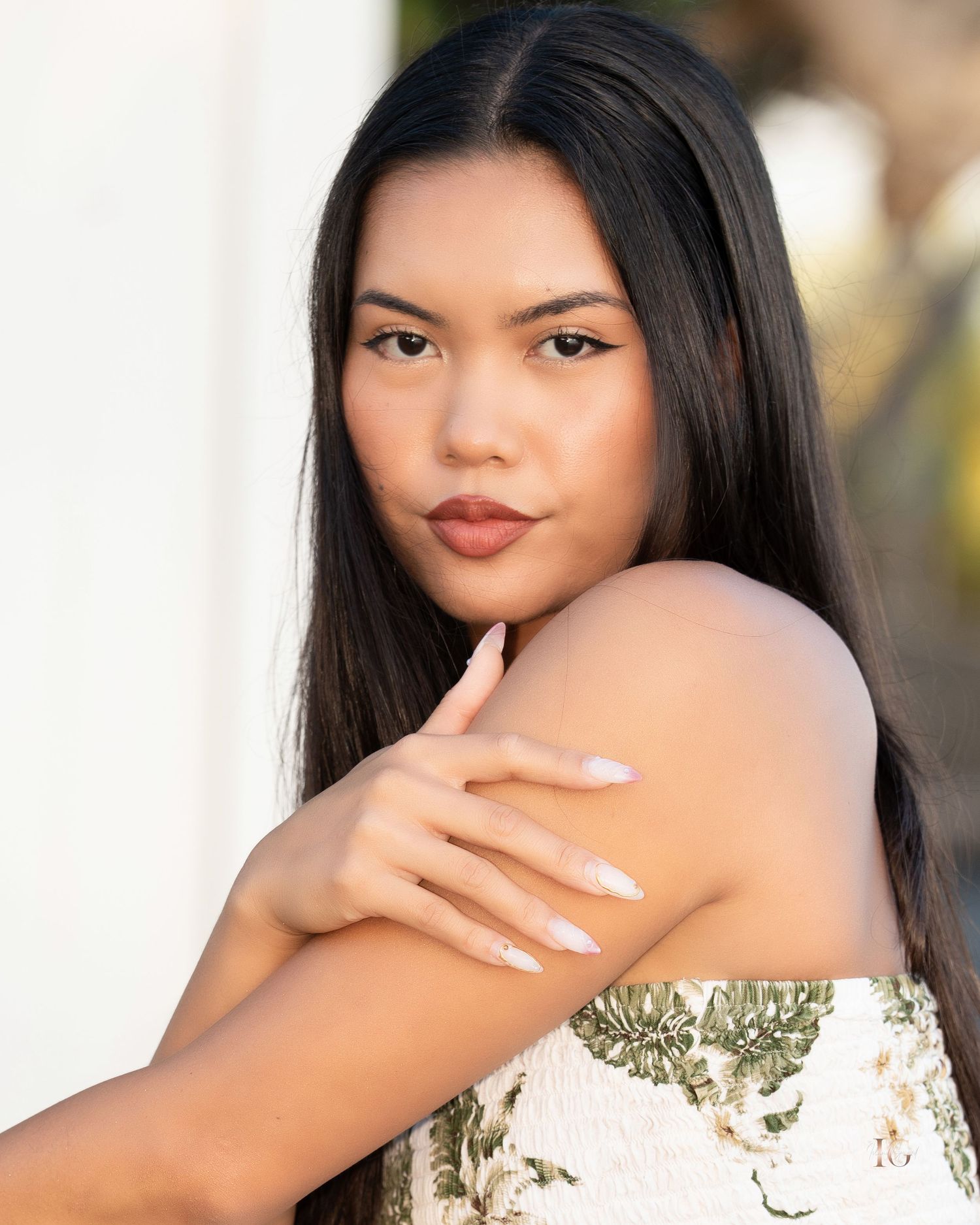 Portrait of a young woman with long straight black hair wearing a white floral dress and white manicured nails.