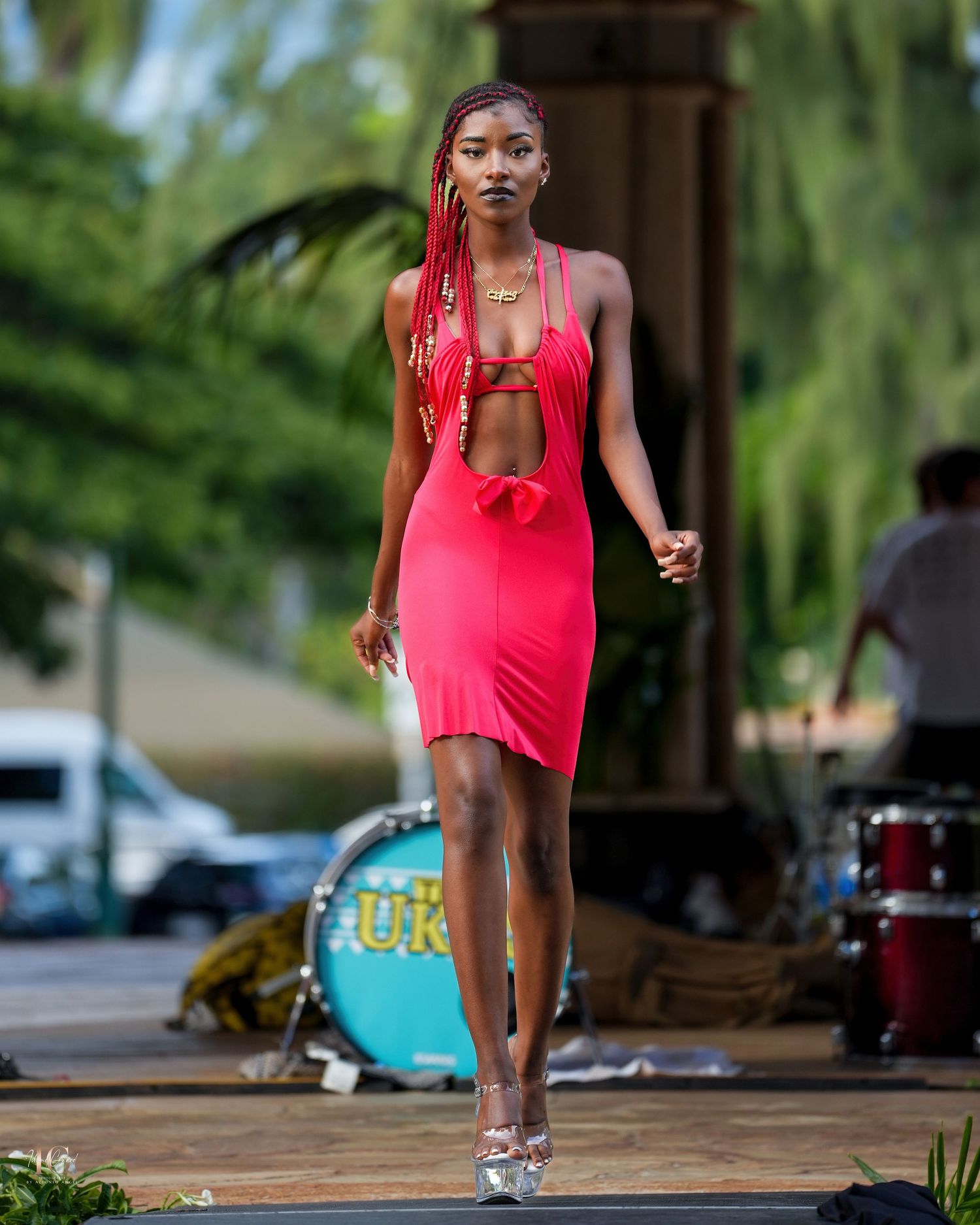 A person in a bright red outfit performs a dynamic dance move on an outdoor stage or platform.