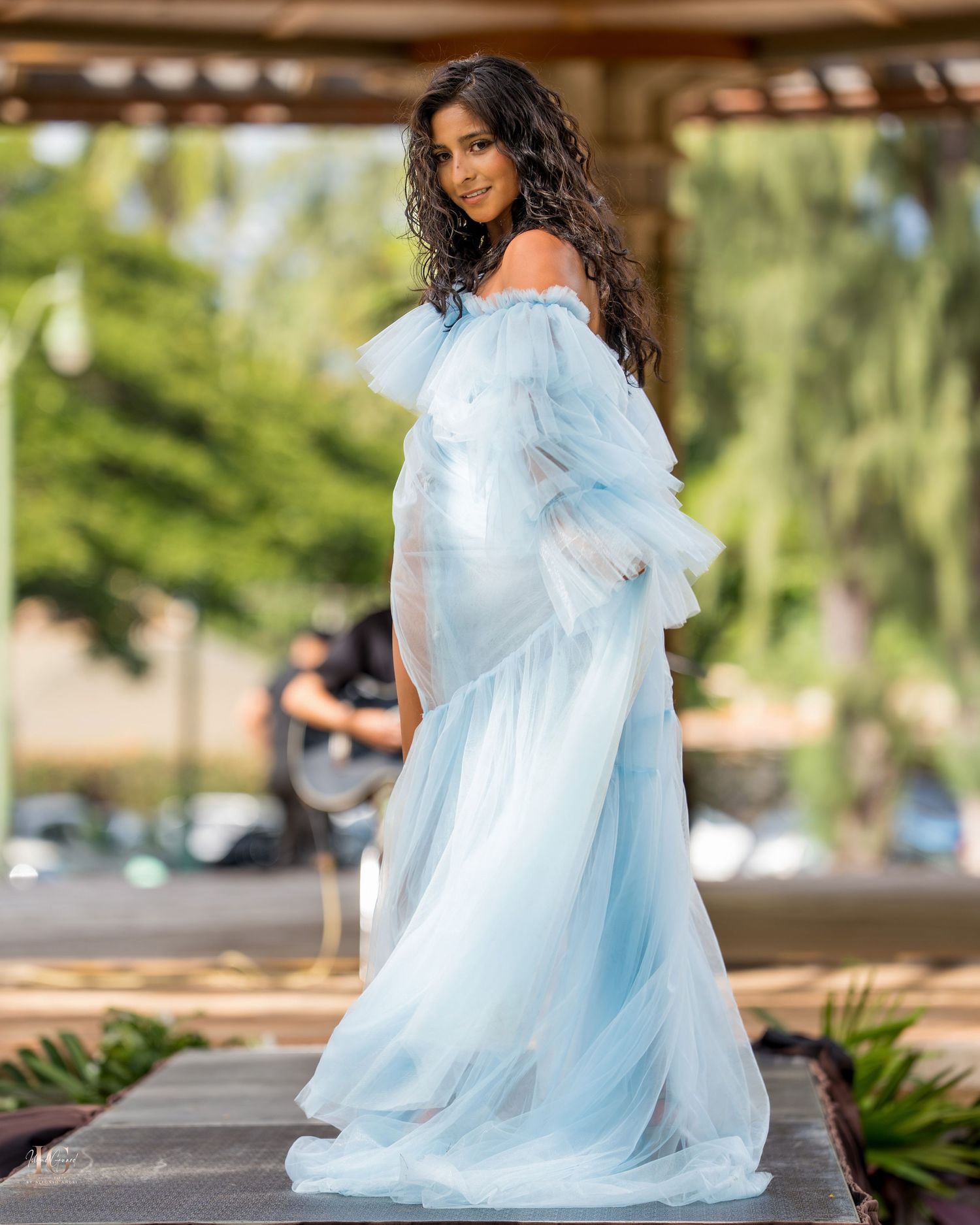 A flowing light blue tulle maternity gown photographed in an outdoor garden setting with natural lighting.