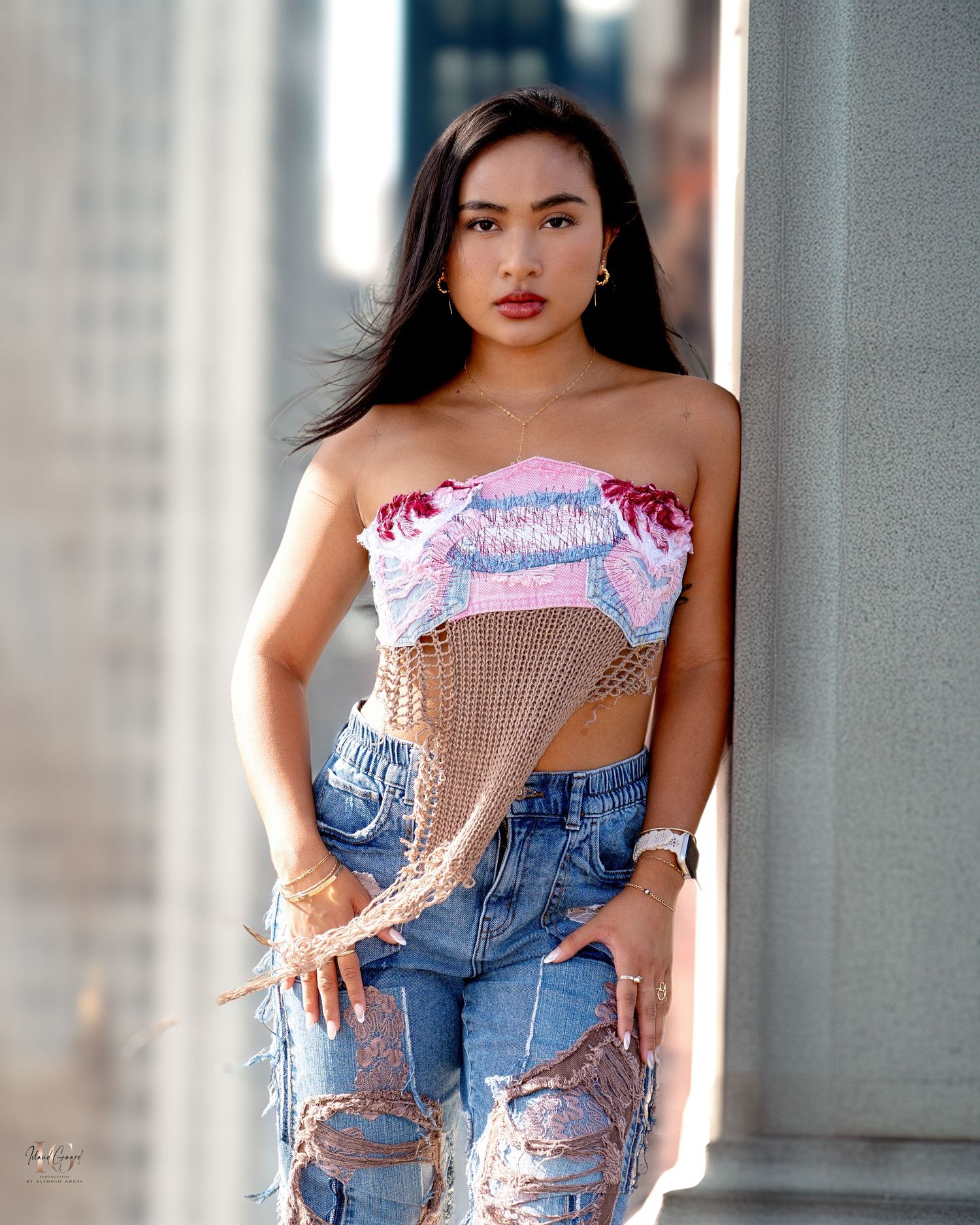 A fashion portrait showing someone in ripped jeans and a pink crop top standing against a concrete wall.