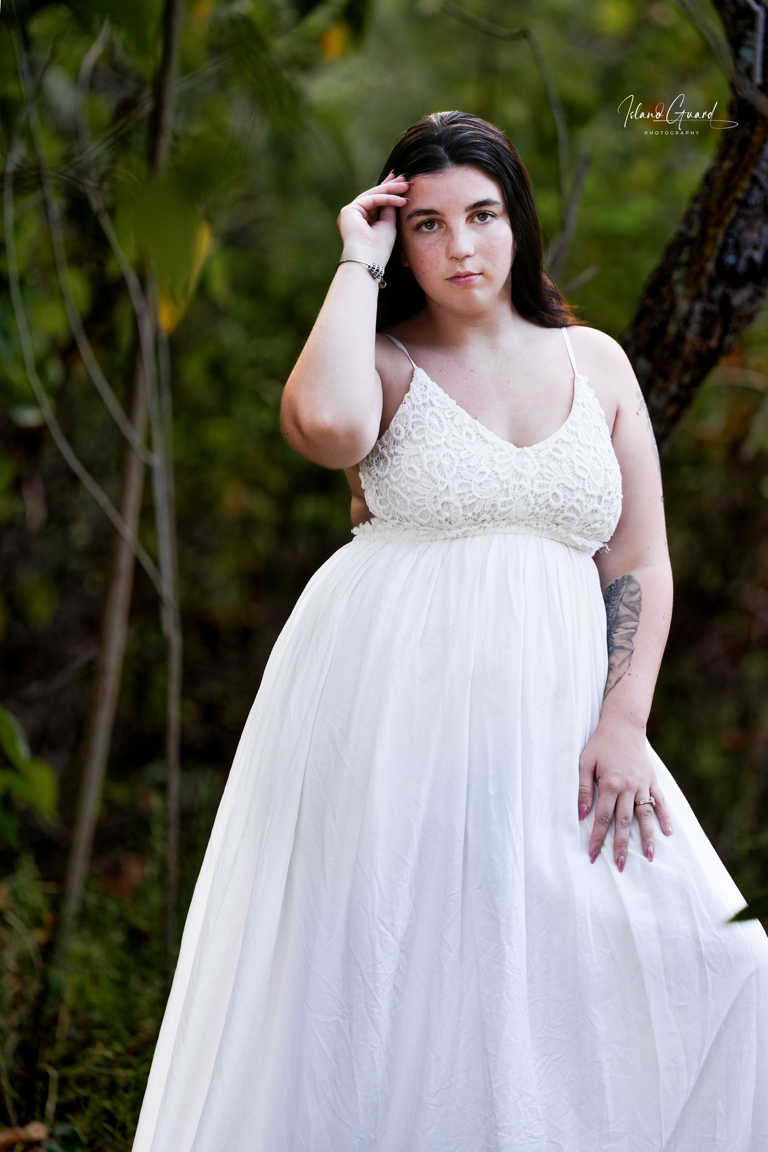 A person in a flowing white empire waist dress poses gracefully outdoors against a natural woodland backdrop.