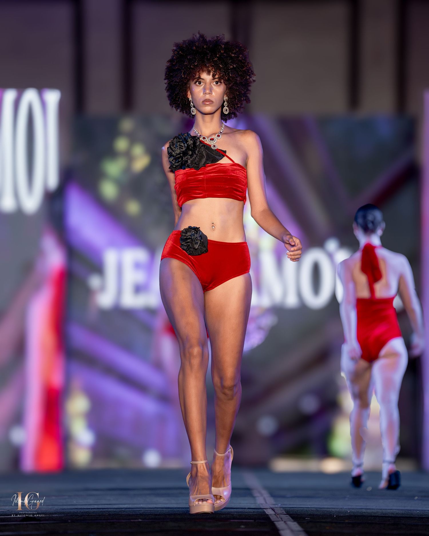 Red two-piece swimwear with black floral accents displayed at fashion show.