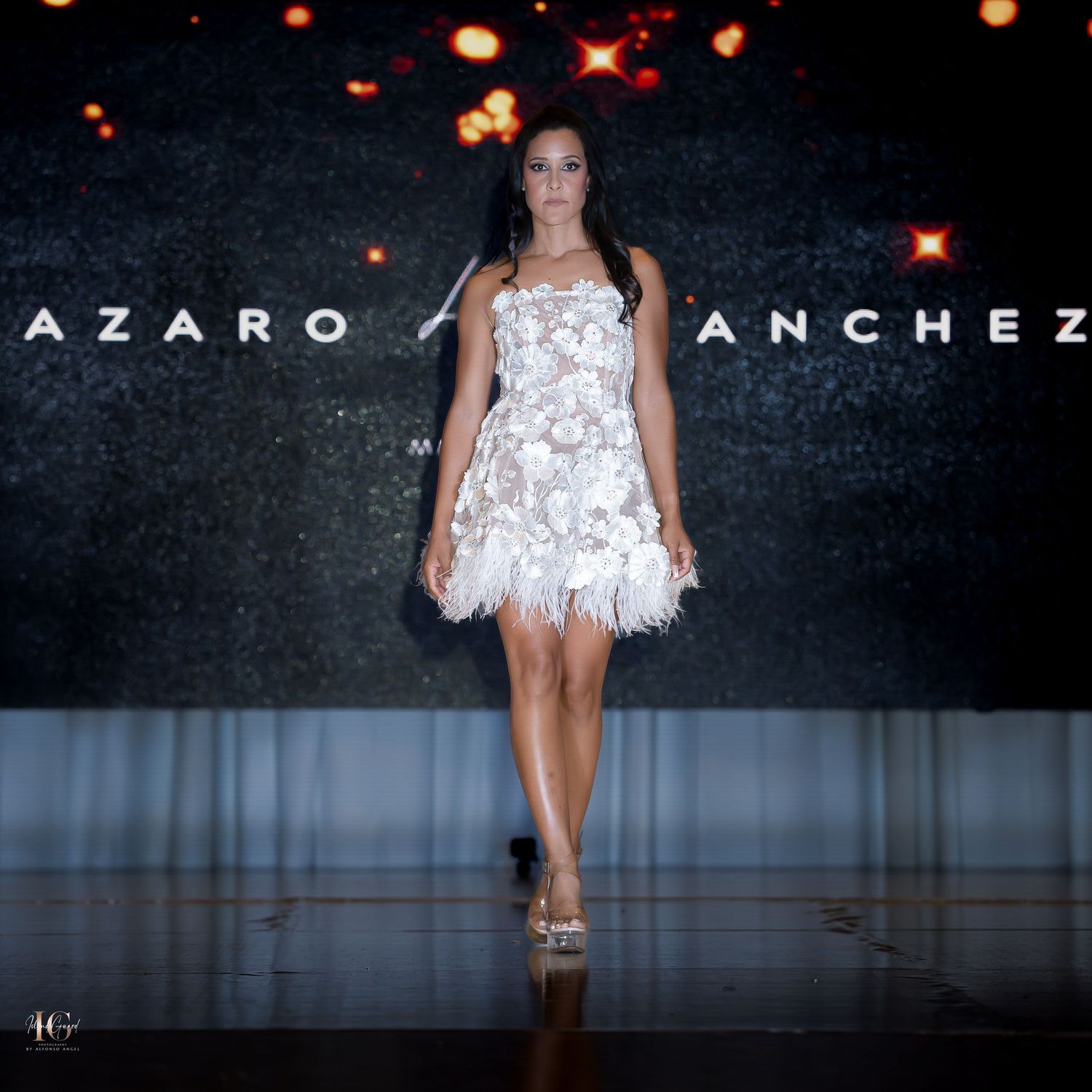 White evening gown with intricate lace detailing on display at Lazaro Sanchez fashion show.