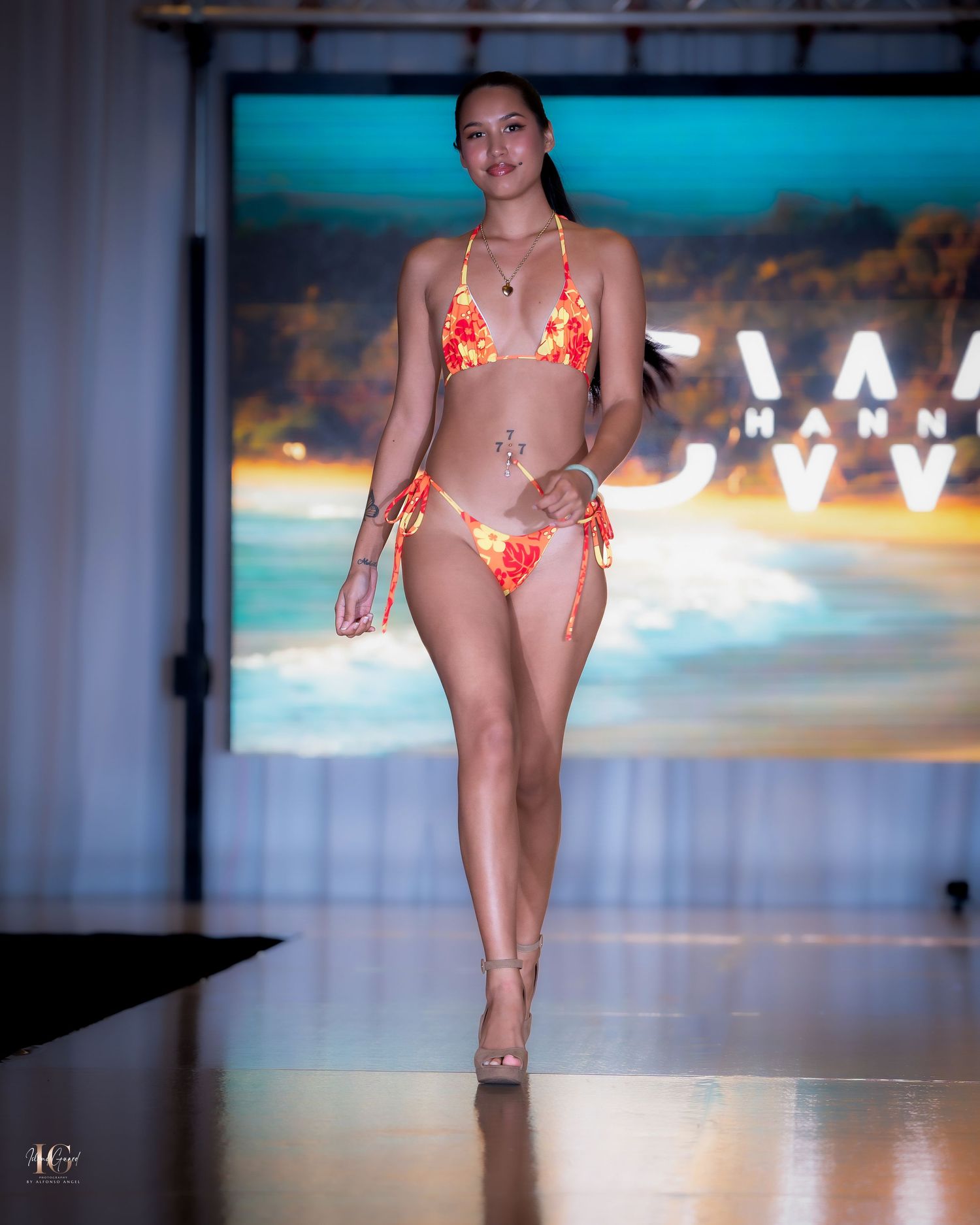 Swimsuit model walks runway in red bikini with tropical beach background display.
