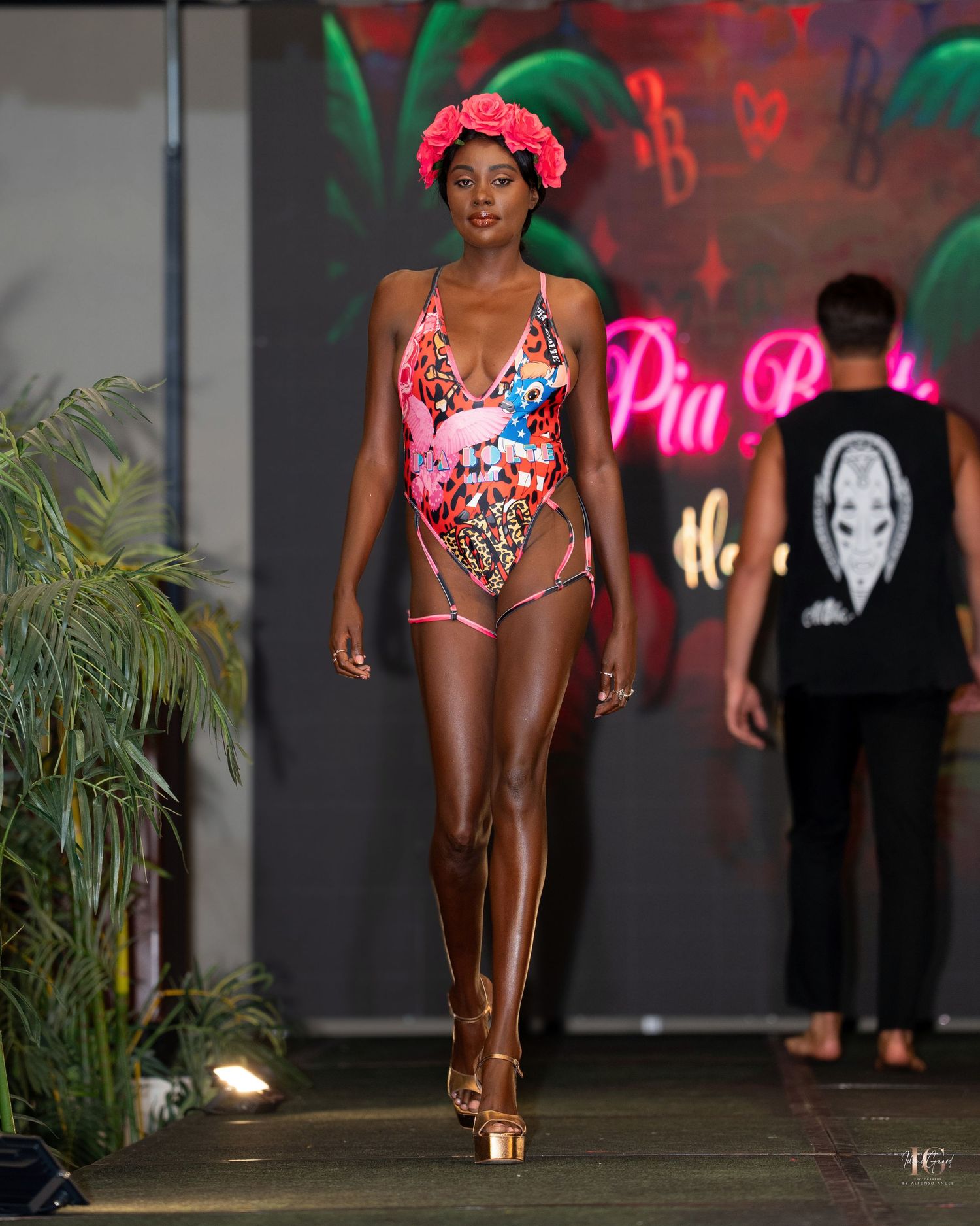 Models walking the runway in vibrant swimwear against a dark backdrop with neon lighting.