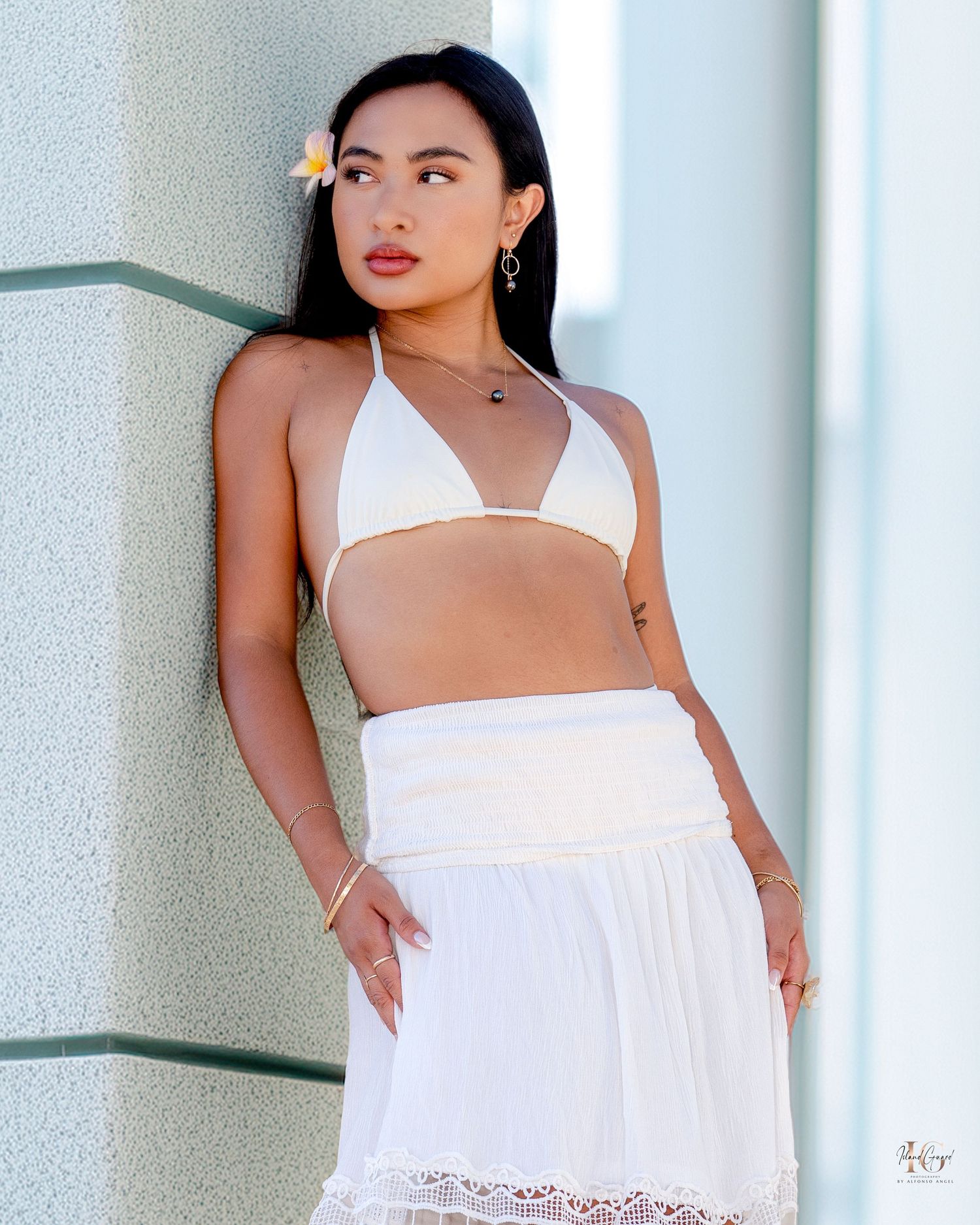 Model posing in a white two-piece outfit with high-waisted skirt and crop top against a light wall in natural lighting.